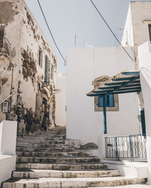 Stairway leading up to a white building with blue accents in a sunlit street.