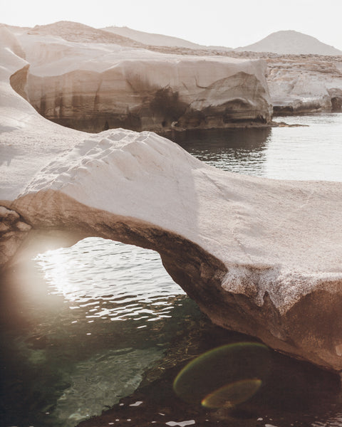 Natural rock arch over a body of water with sunlight filtering through