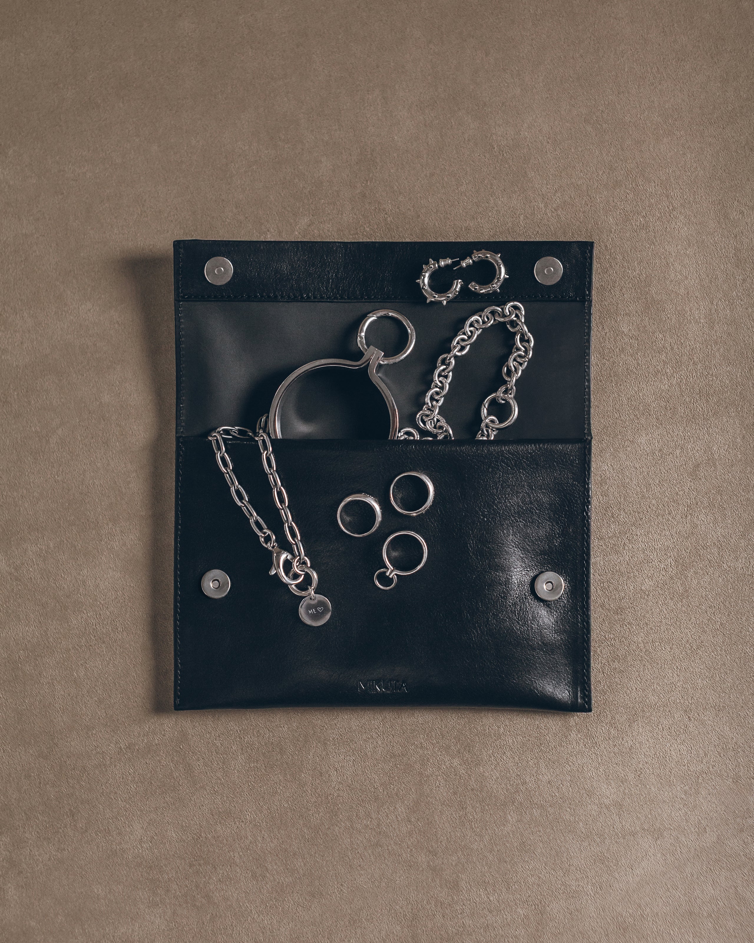 Black leather pouch with silver handcuffs and chains on a beige background