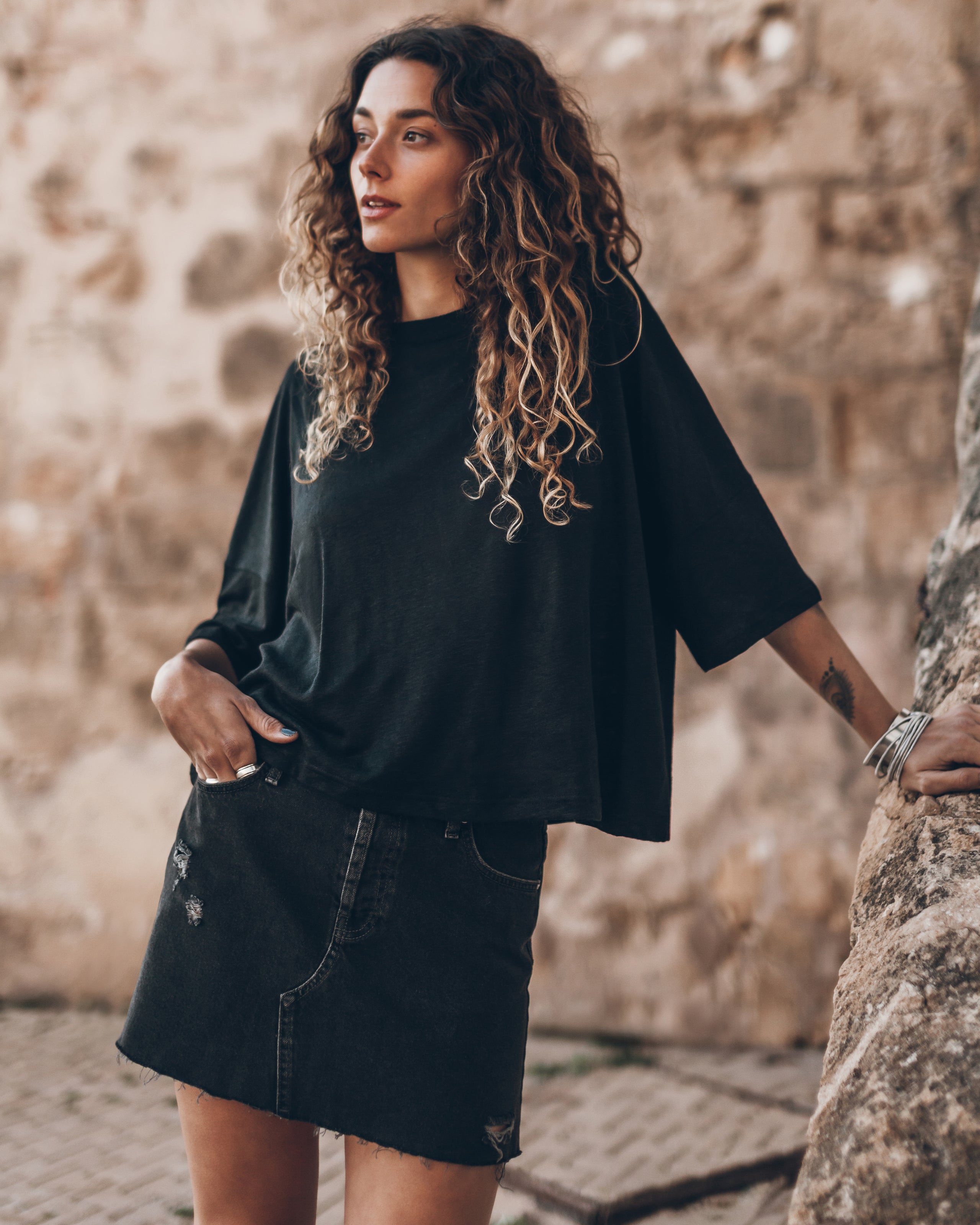 Black loose-fit linen t-shirt with elbow-length sleeves worn with a black denim skirt.
