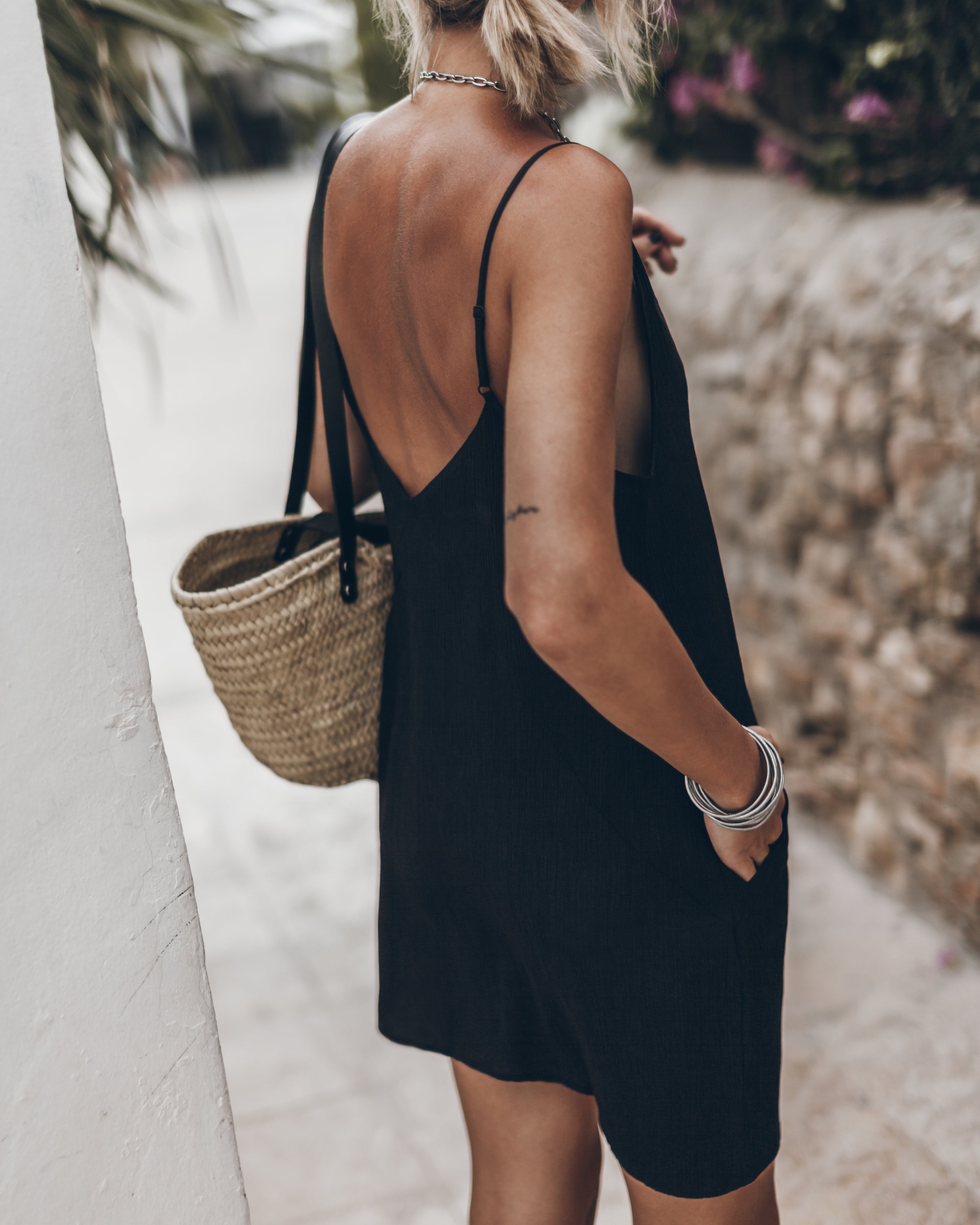 Woman in a black dress with a straw bag and silver bracelets.
