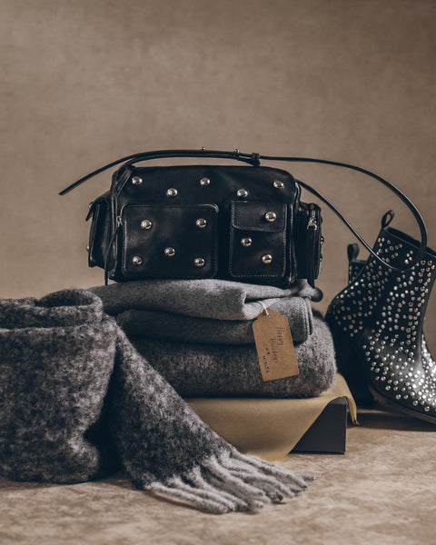 Black studded handbag, gray scarf, and black studded boots on a beige surface.