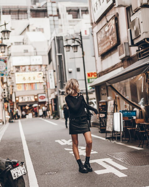 Person walking down a busy street in an urban setting with buildings and signs in the background.