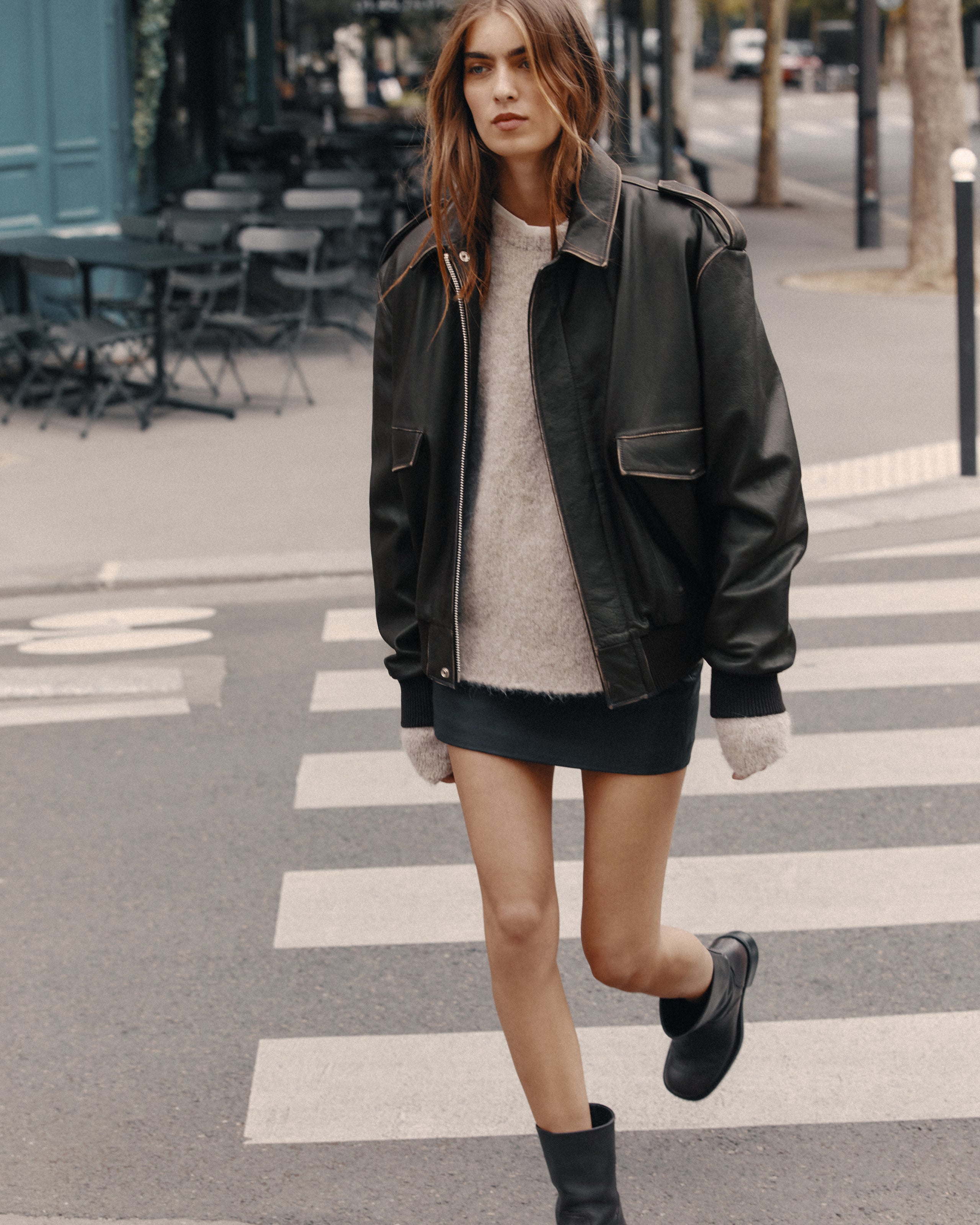 Woman crossing a street wearing a black leather jacket and black boots.