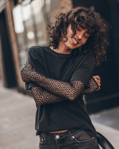 A woman wearing a black crewneck t-shirt, a black lace long-sleeve and black denim jeans.