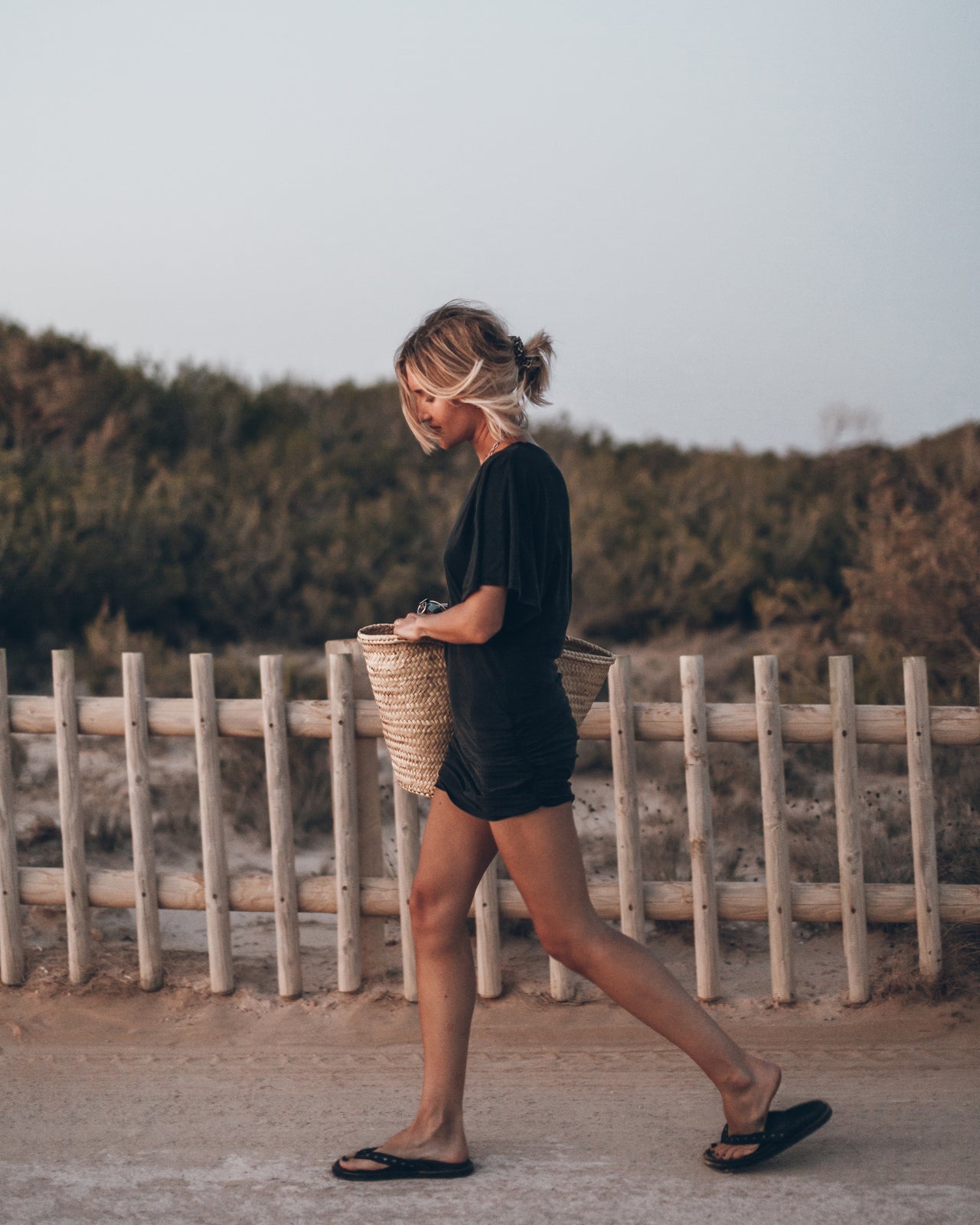 Woman walking on a path with a woven basket, surrounded by greenery.