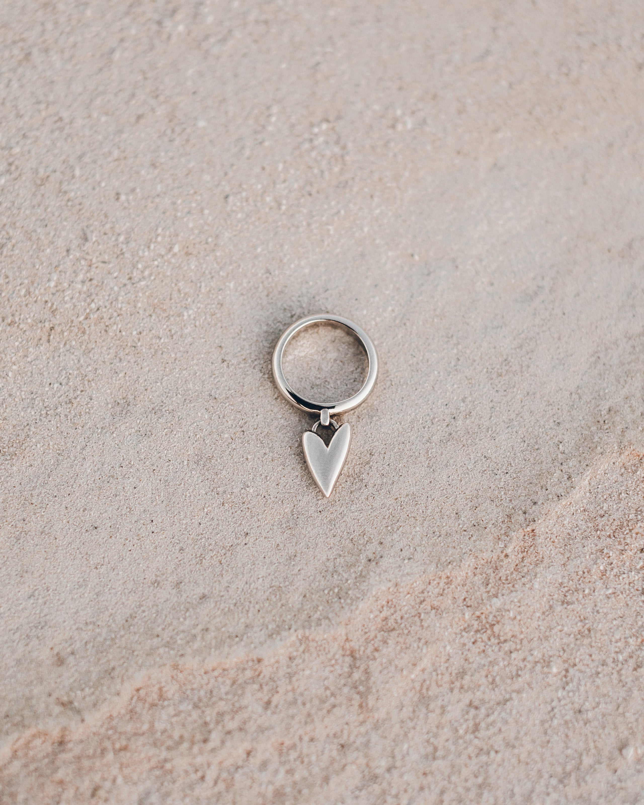 Silver ring with a heart-shaped pendant on a beige surface