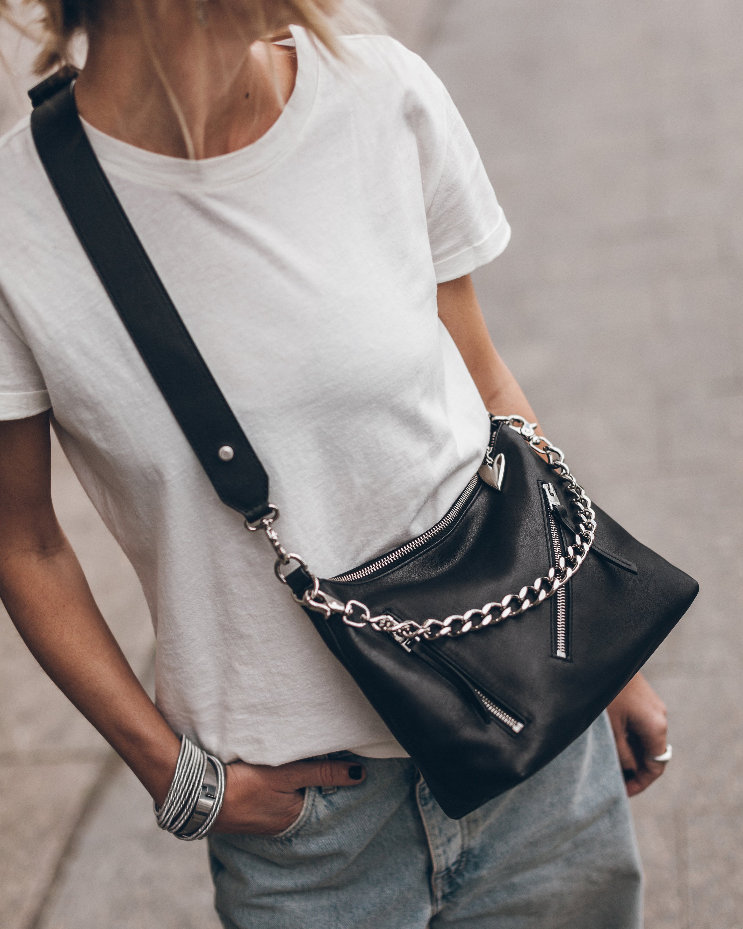 Woman wearing a black handbag with a chain detail, wearing a white t-shirt and blue jeans.