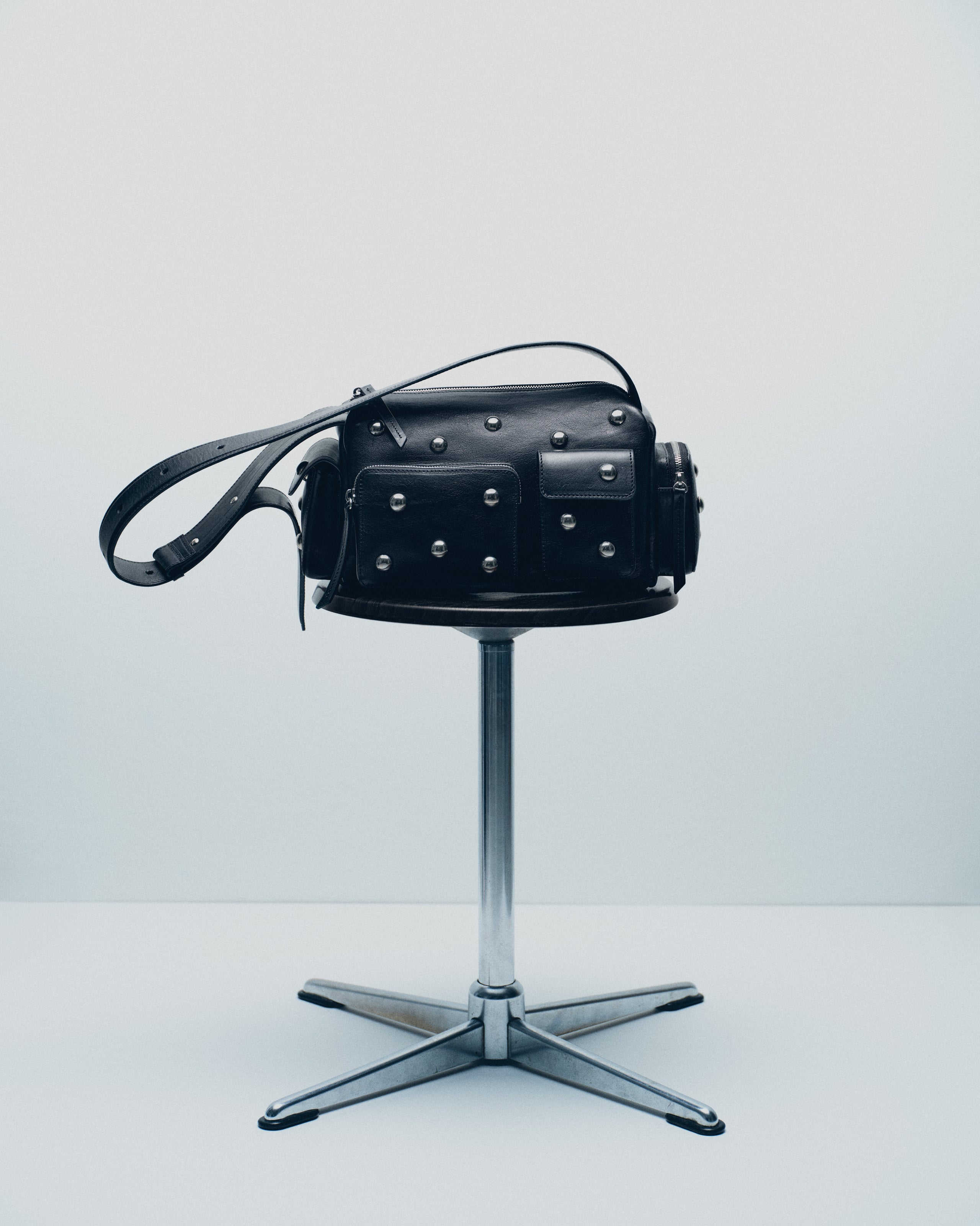 Black leather bag with studs on silver swivel stool.