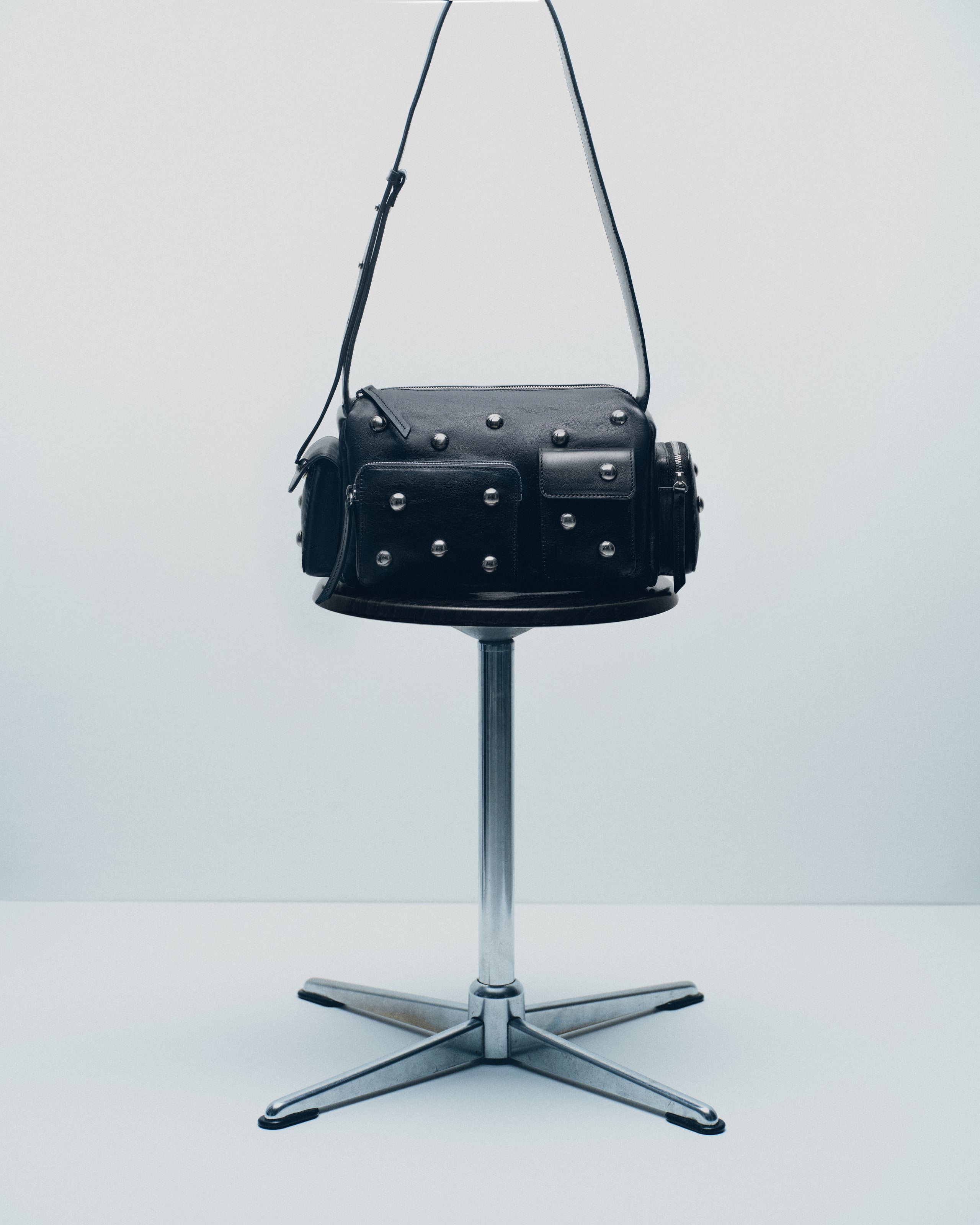 Black leather studded shoulder bag on a metal stool.