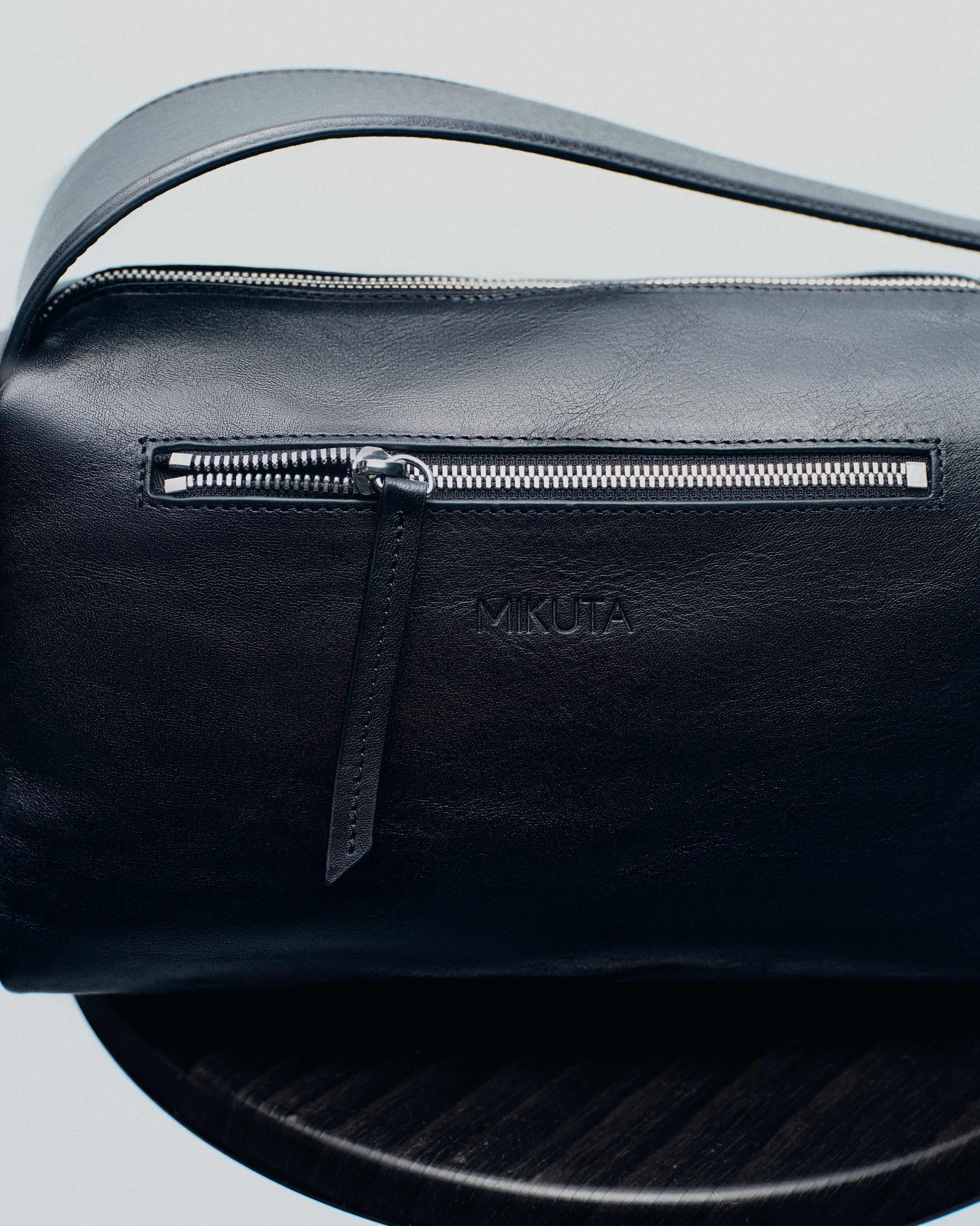 Black leather bag with silver zipper and "MIKUTA" logo.