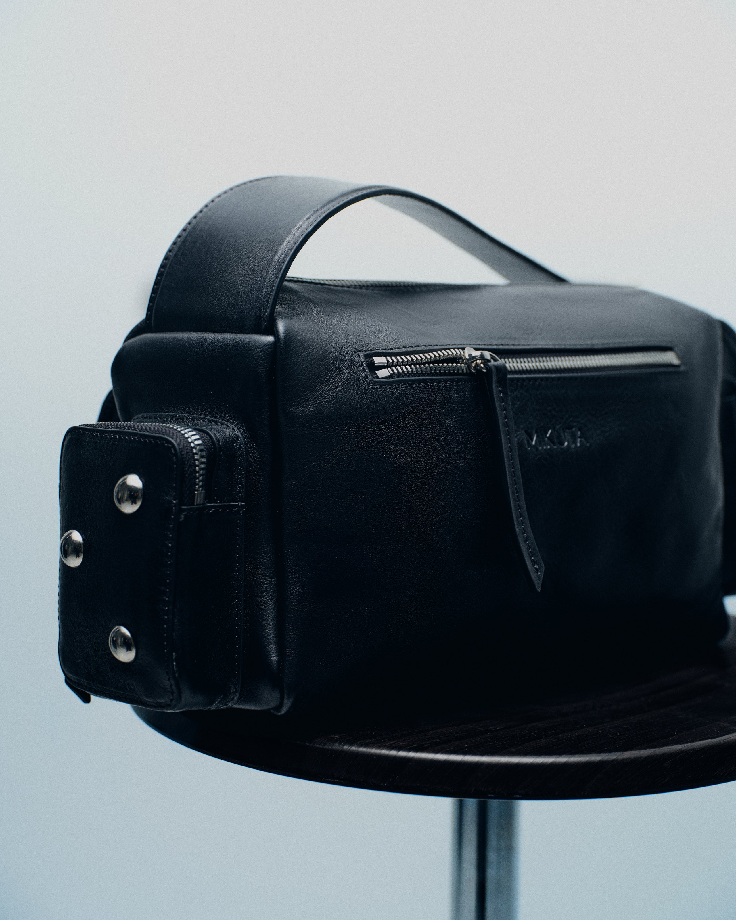 Black leather bag with silver hardware on a stool.