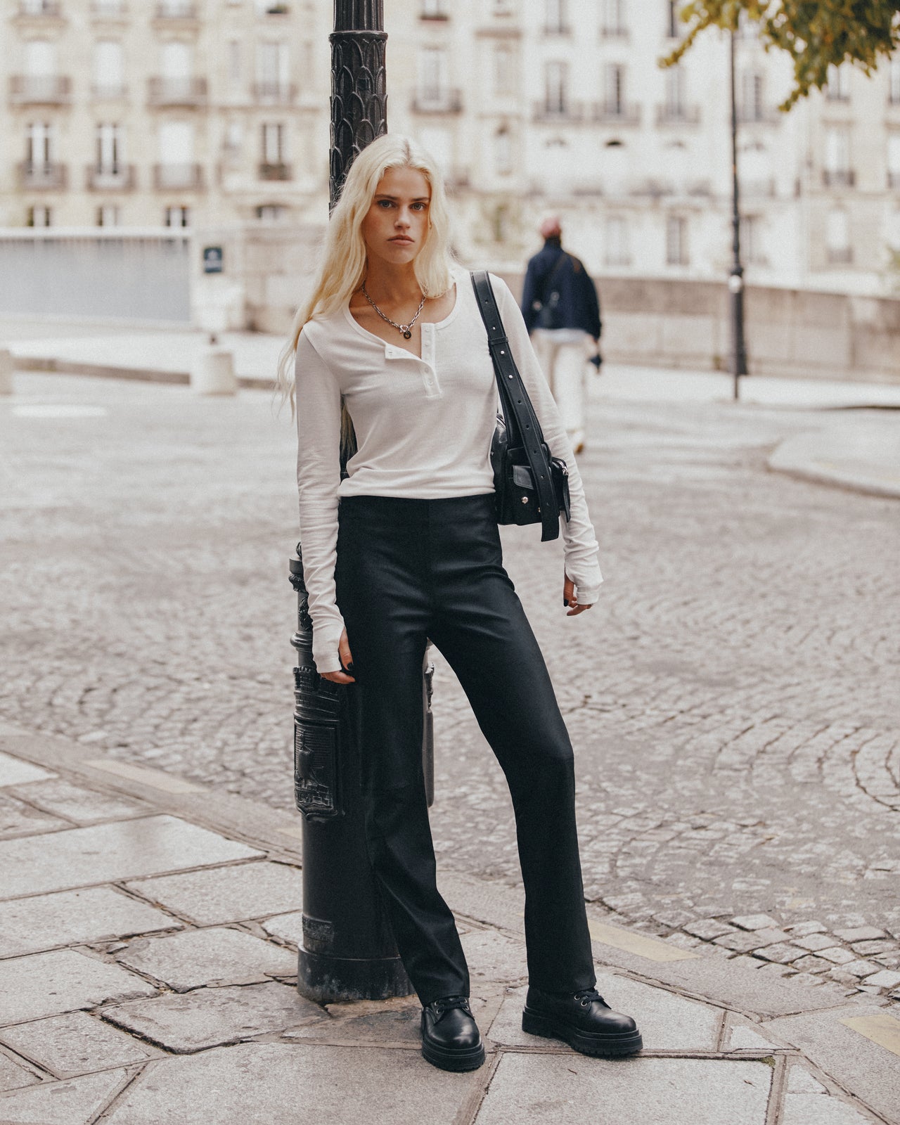 Person wearing a white top and black pants standing on a street.