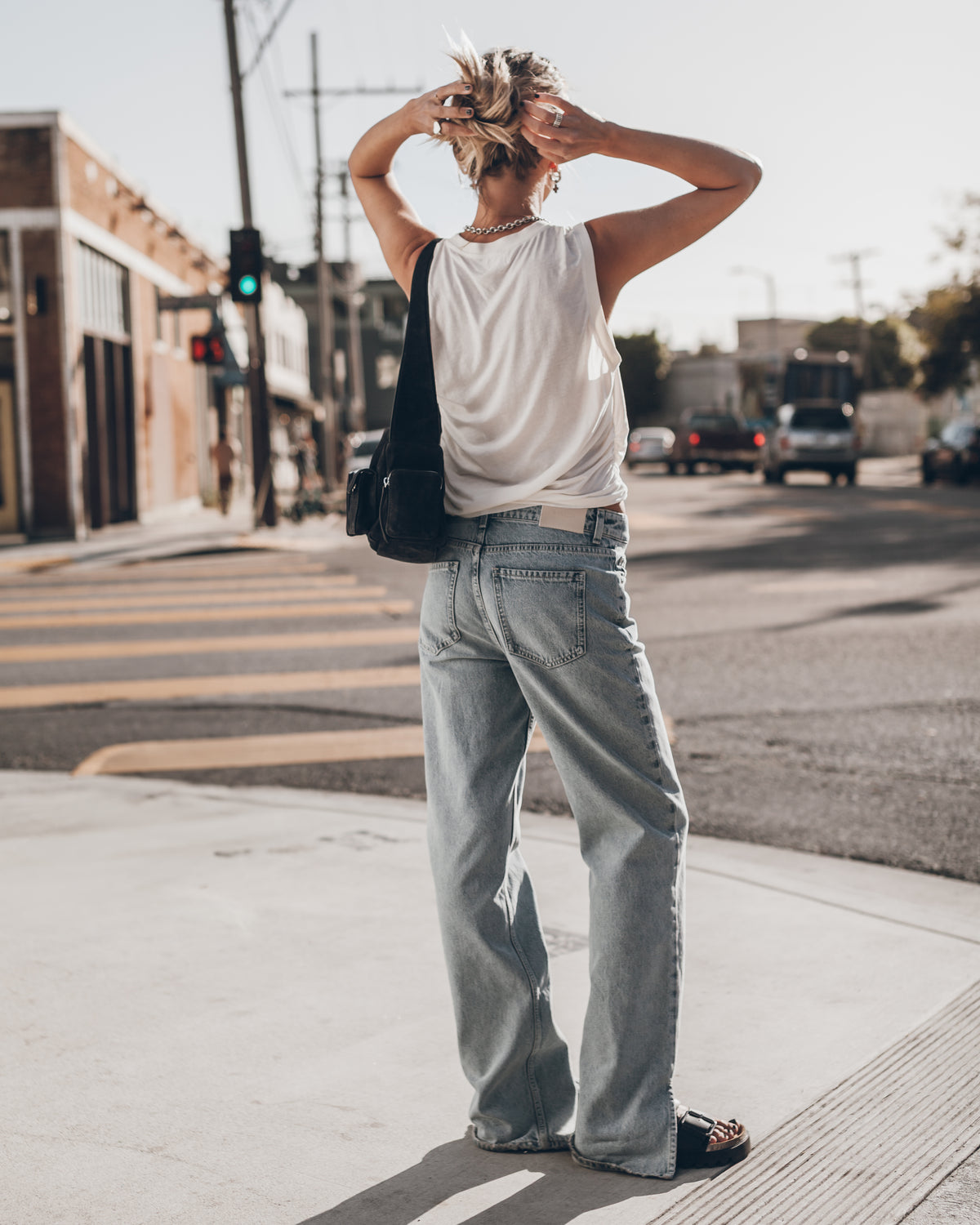 Person wearing a white tank top and light blue jeans standing on a city street.