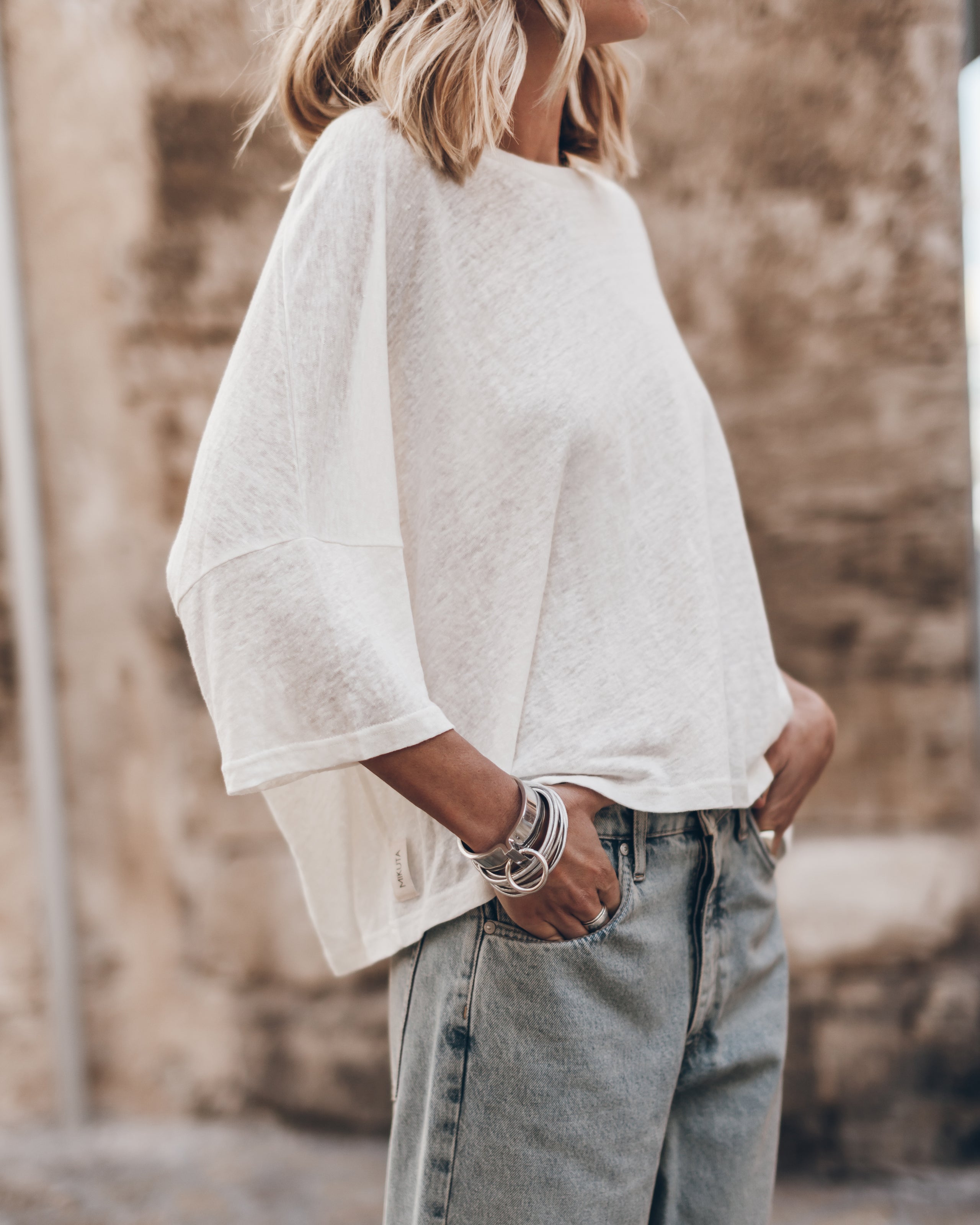 White loose linen t-shirt with wide sleeves paired with light blue jeans and silver bracelets.