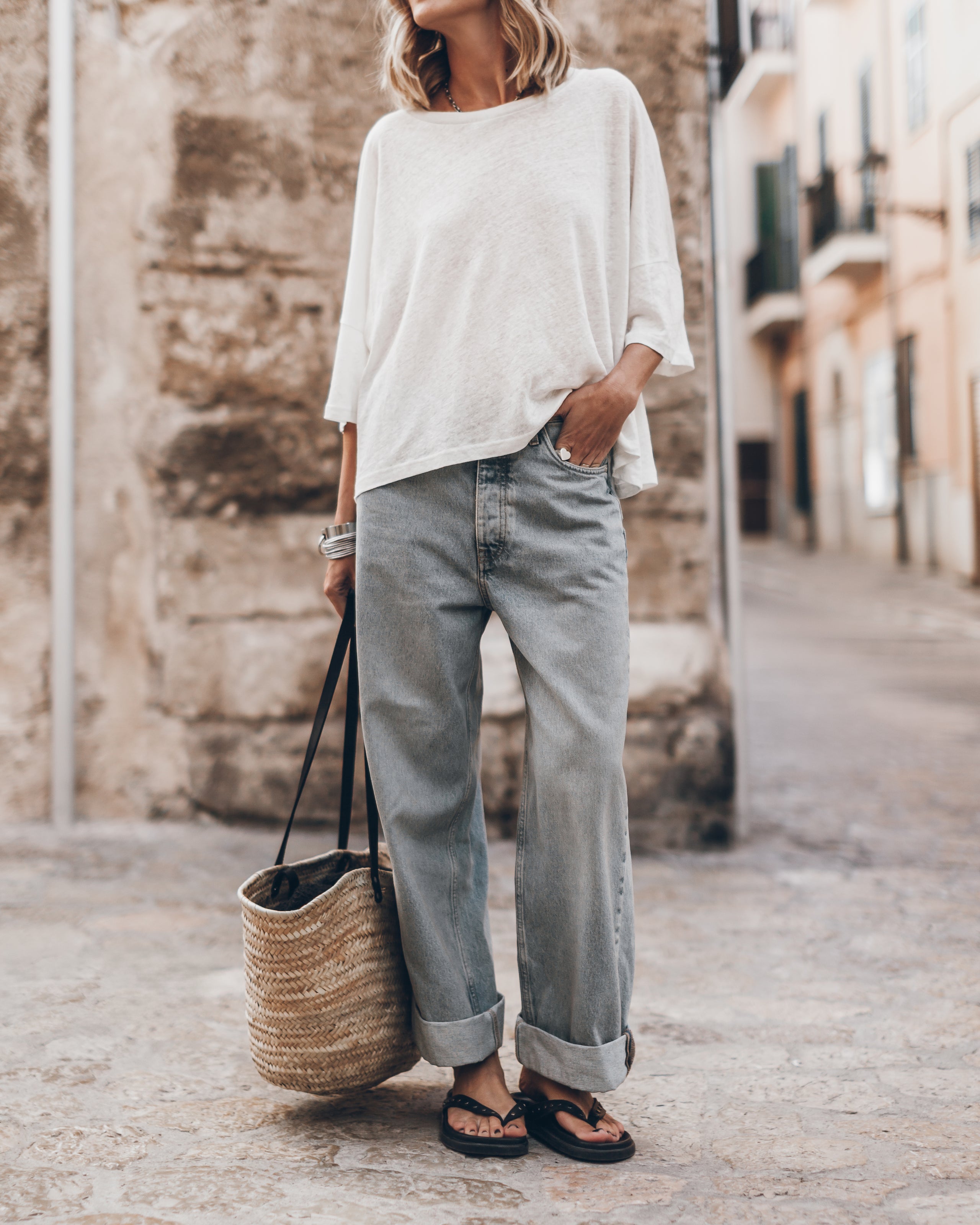 White loose linen short-sleeve t-shirt paired with light-wash cuffed jeans and black sandals, styled with a woven straw tote .