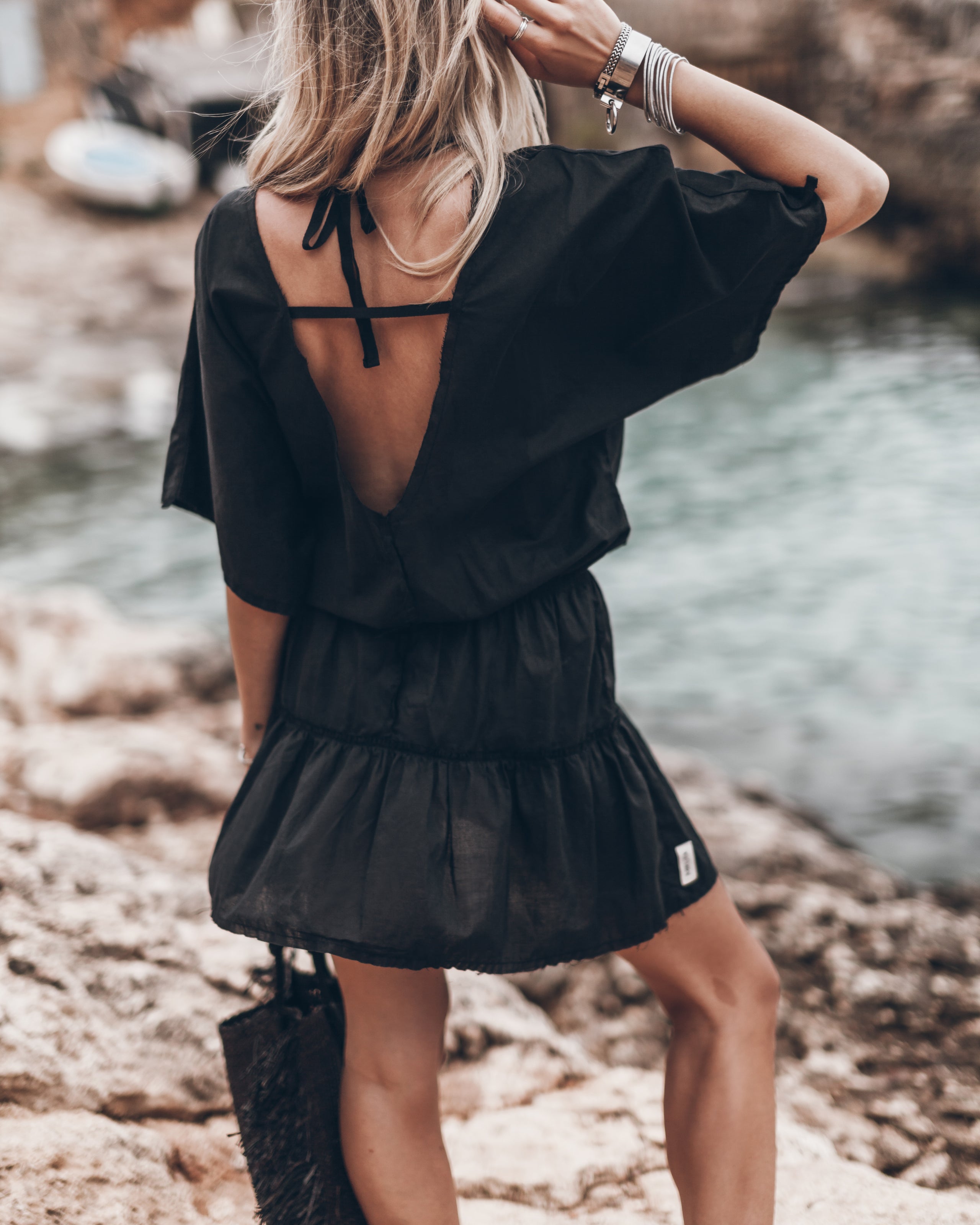 Black short summer dress with deep V-back and loose short sleeves, worn outdoors near water.
