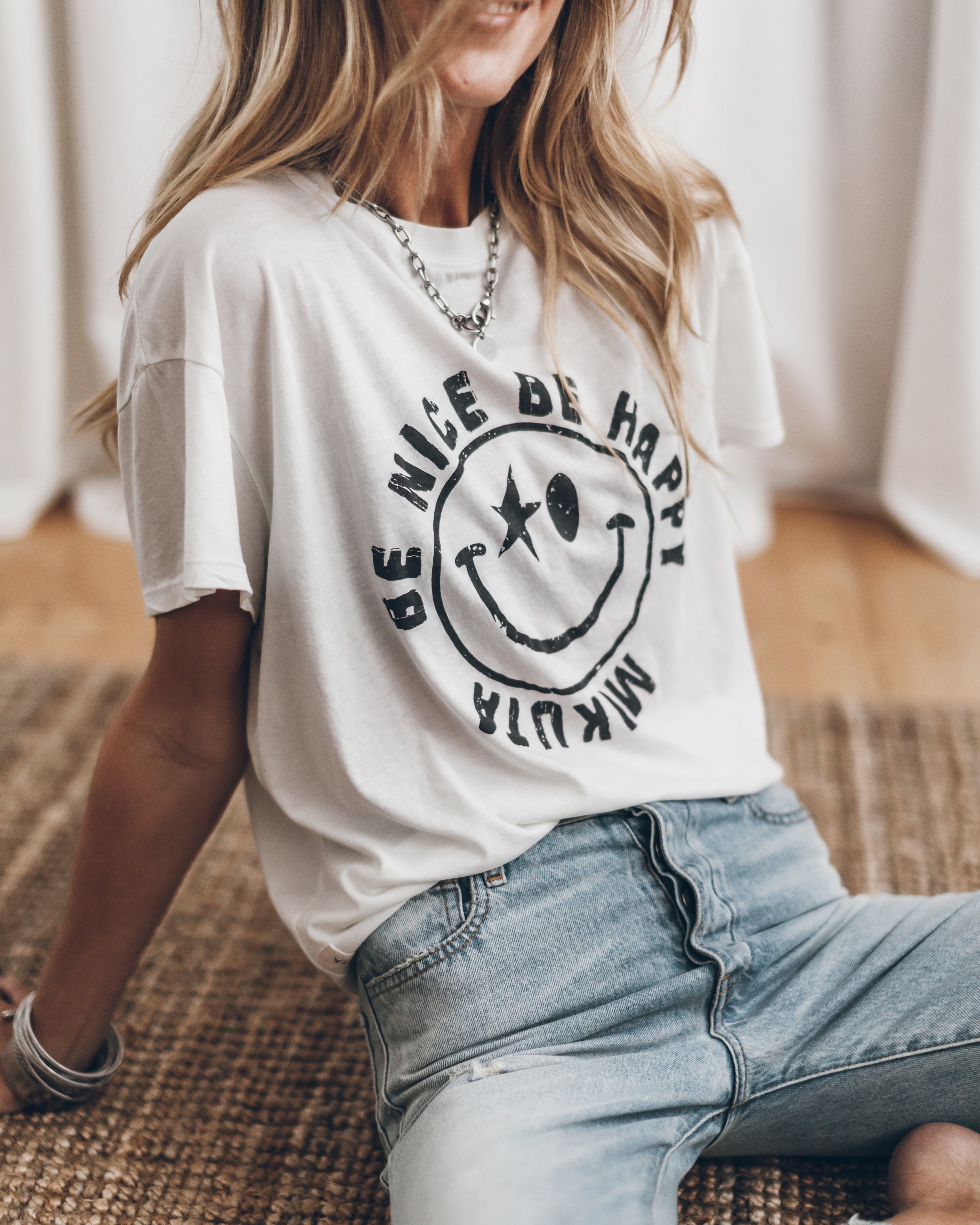 White oversized t-shirt with a black smiley face and circular text, paired with light blue jeans.