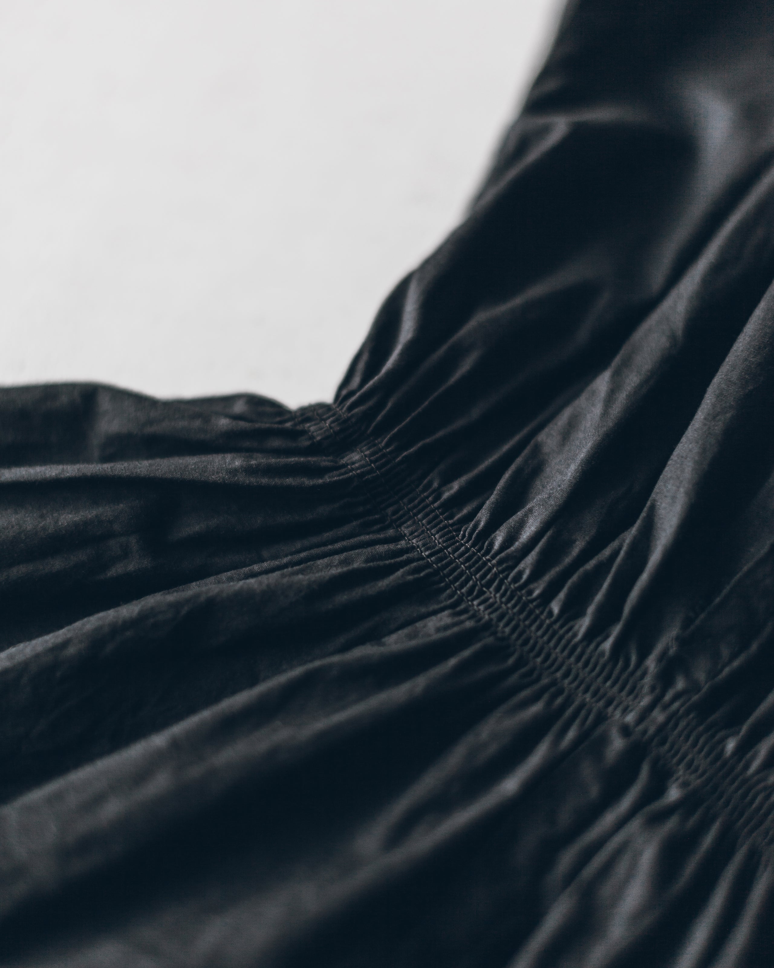 Black satin-like fabric with gathered elastic waist detail on a dark summer dress.