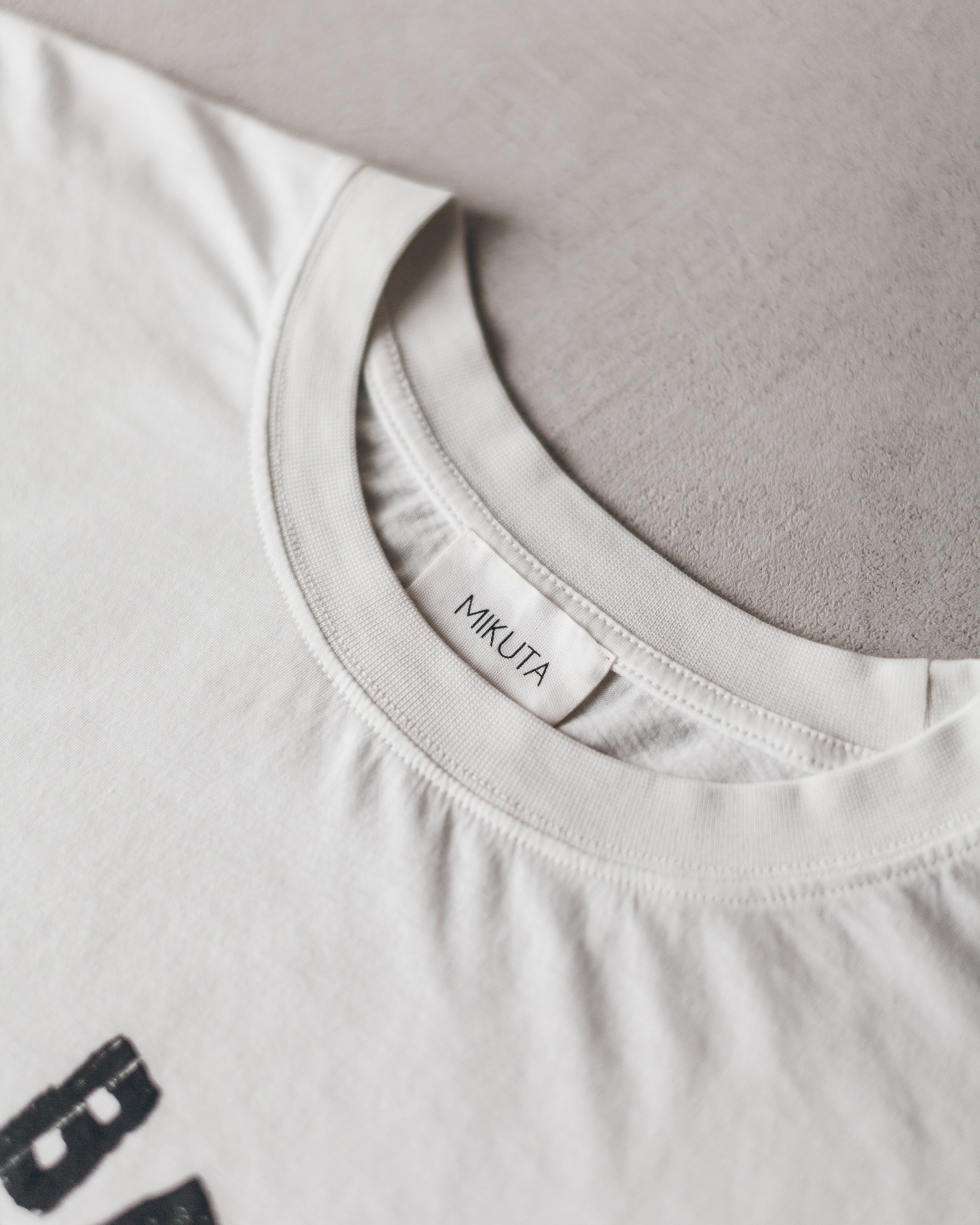 White crew neck T-shirt with small black smiley graphic and Mukta label inside collar.