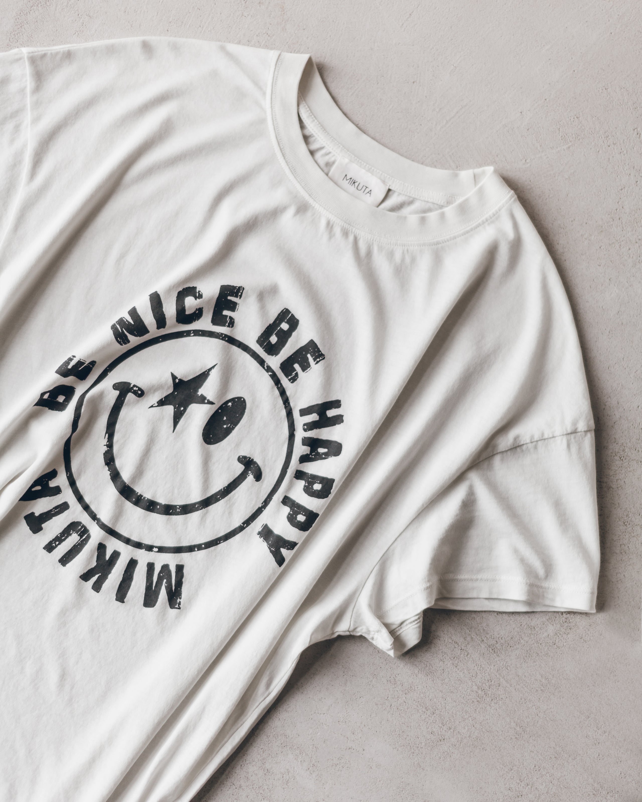 White cotton T-shirt with a black smiley face and "Be Nice Be Happy" text design.