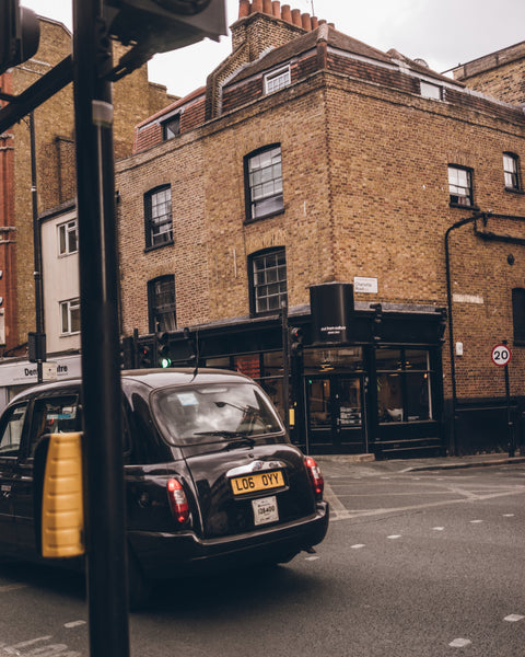 A black London cab parked on a city street in front of a brick building.