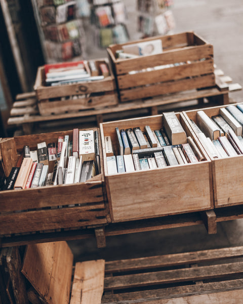 Rustic wooden crates filled with books stacked on wooden pallets in a shop or storage area.
