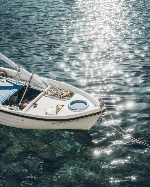 White boat floating on clear blue water with sunlight reflecting off the surface