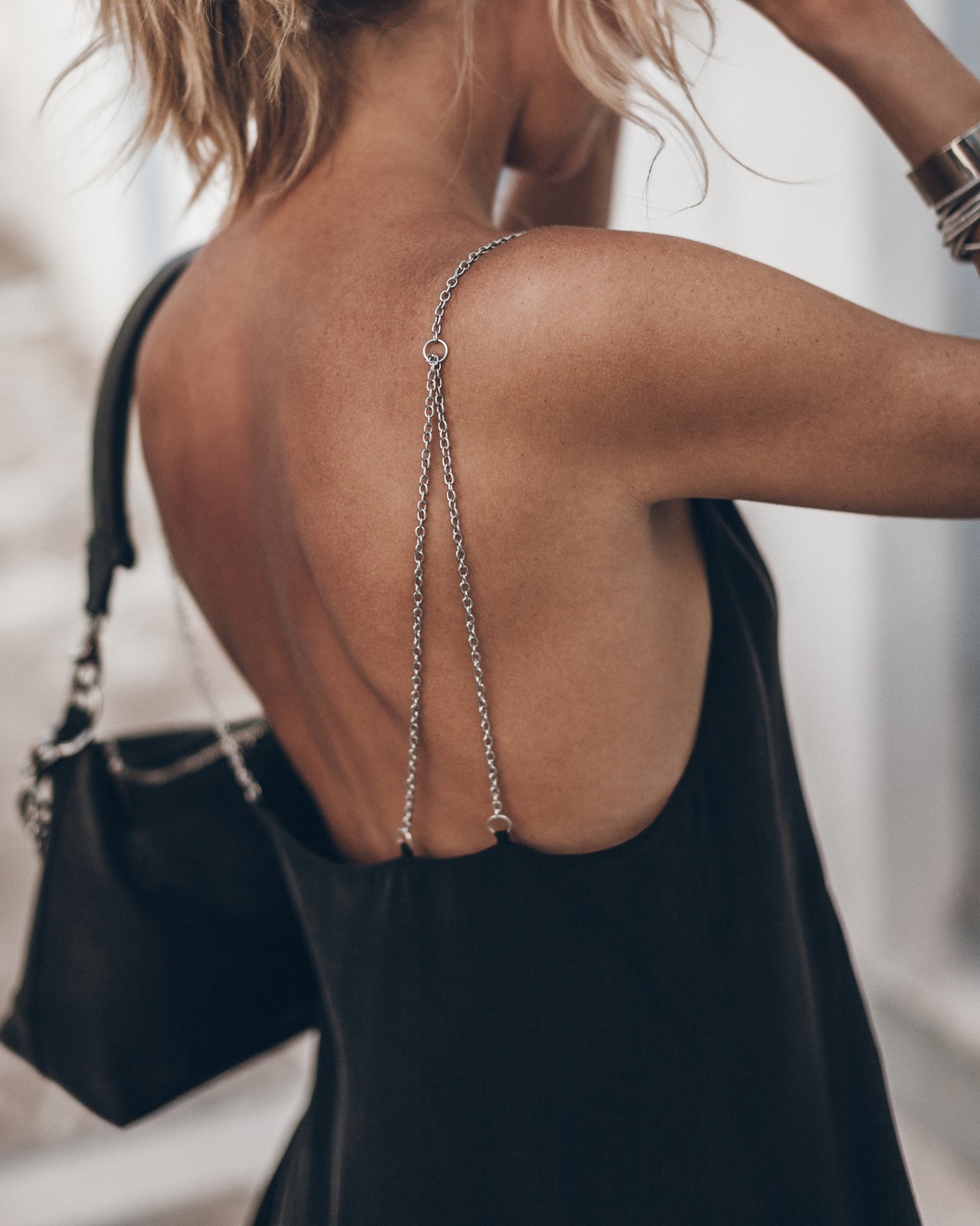 Woman wearing a black dress with an open back and chain detail, holding a black handbag.