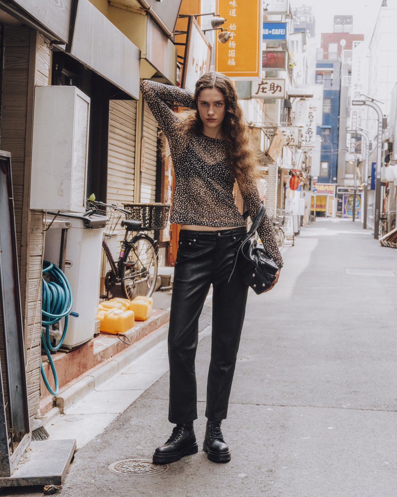 Person standing on a city street wearing a patterned sweater and black pants.