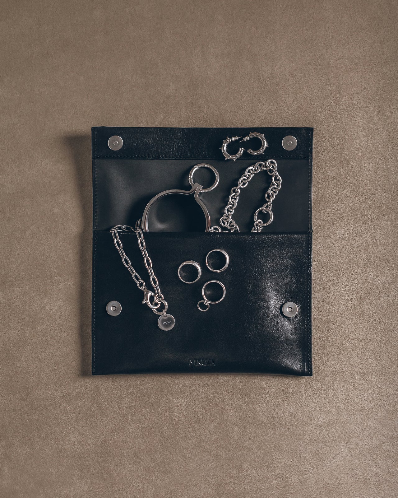 Black leather pouch with silver handcuffs and chains on a beige background