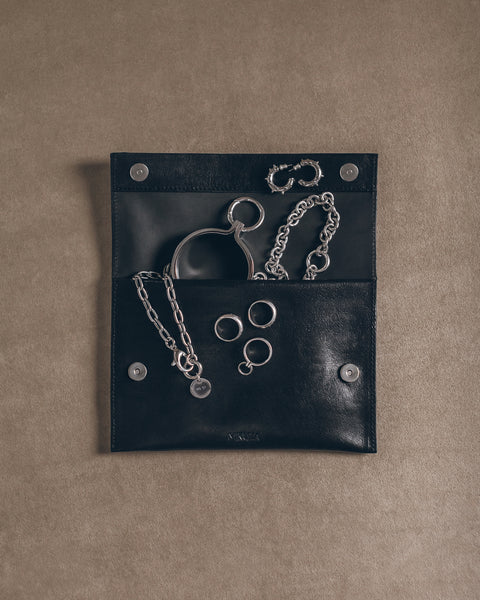 Black leather pouch with silver handcuffs and chains on a beige background