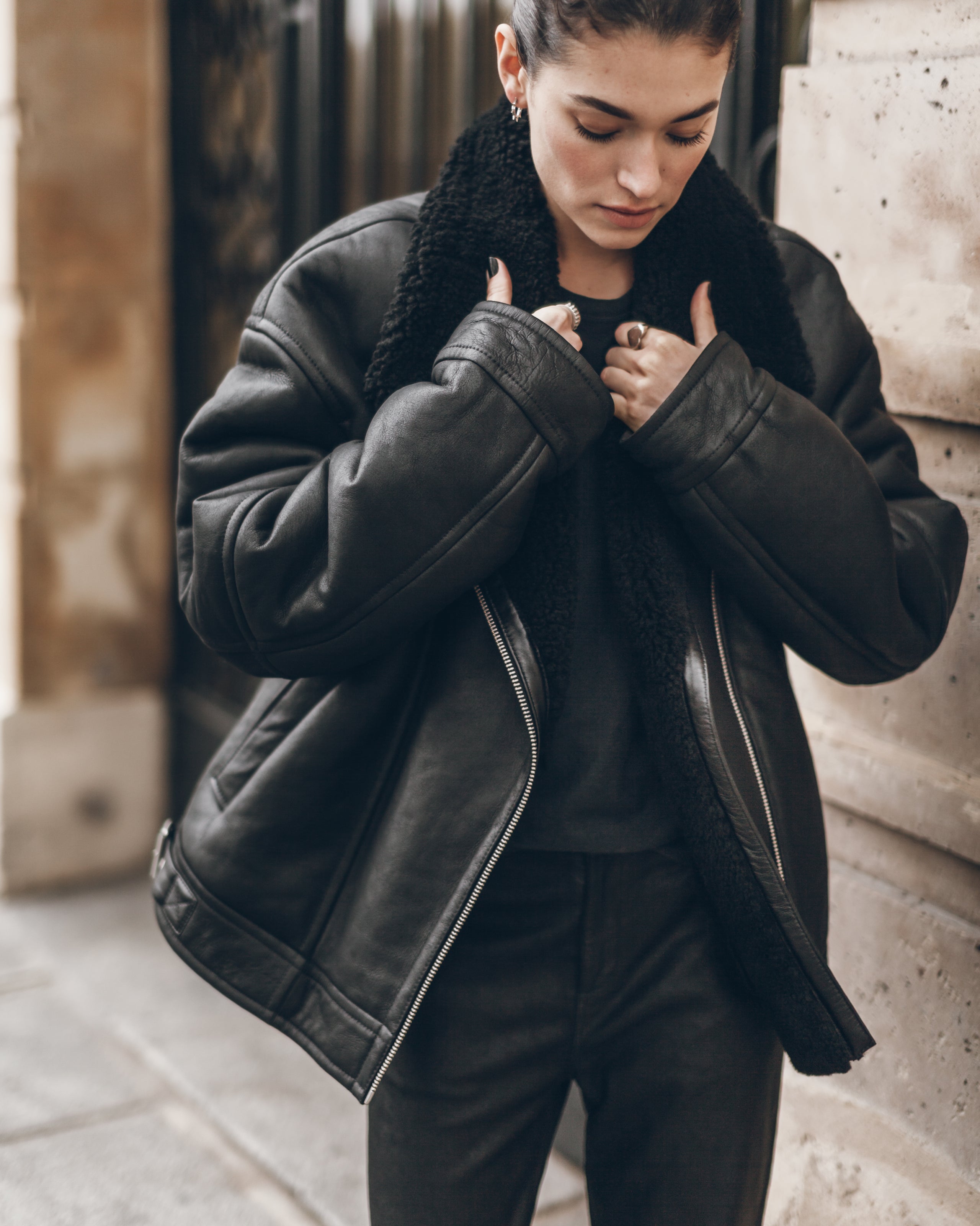 Person wearing a black leather jacket with fur lining in an urban setting