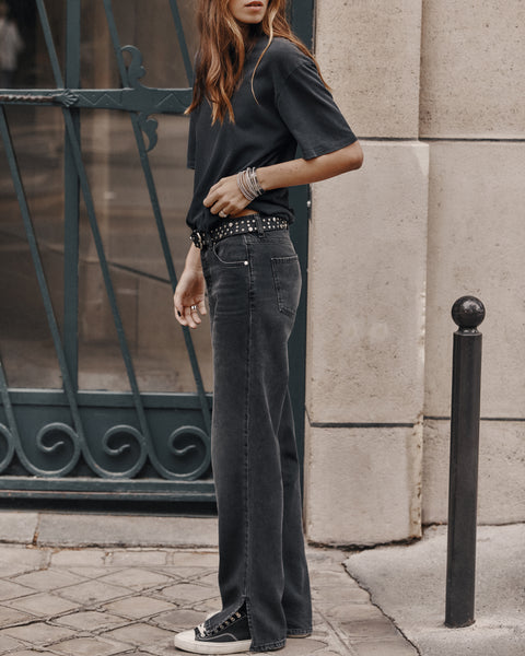Person wearing a black t-shirt and jeans standing on a street with a decorative metal gate in the background.