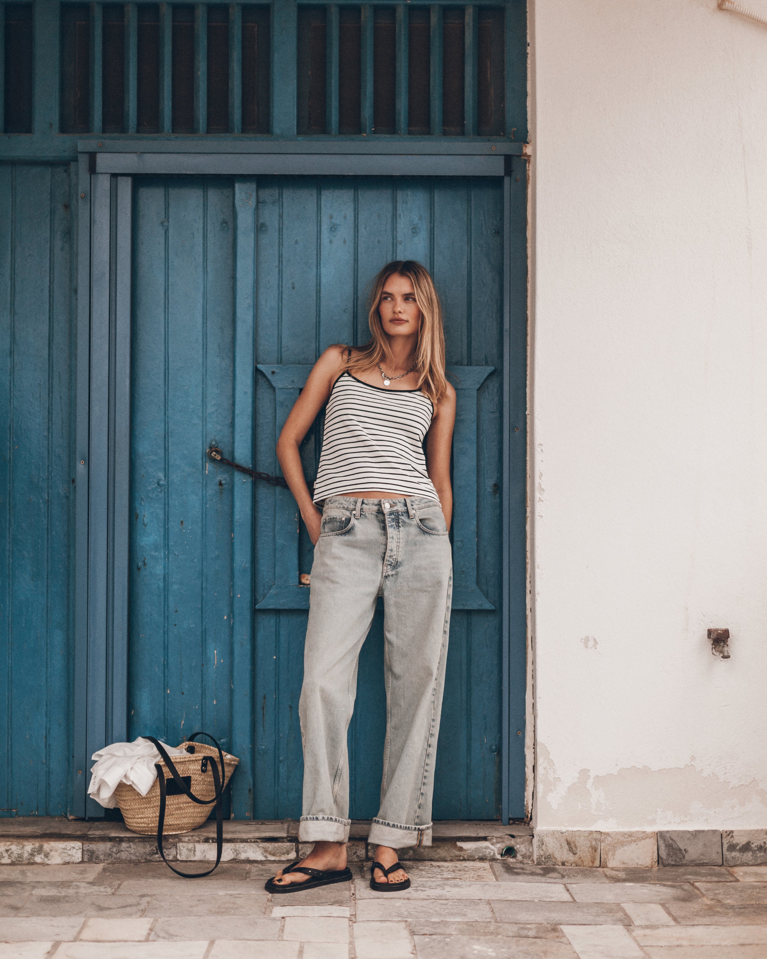 Woman wearing a striped tank top and jeans against a blue wall.