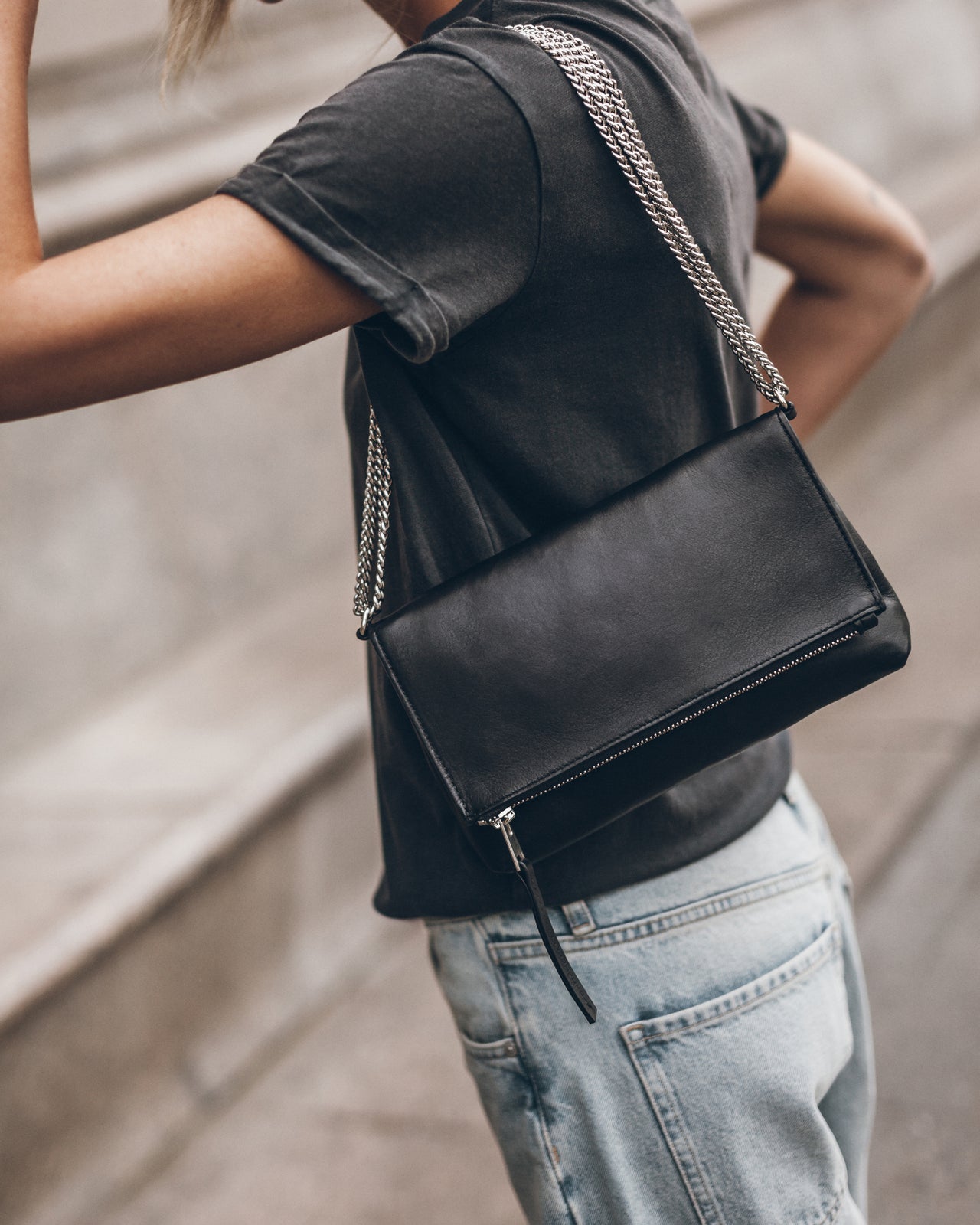 Person wearing a black t-shirt and light blue jeans, holding a black clutch with a chain strap.