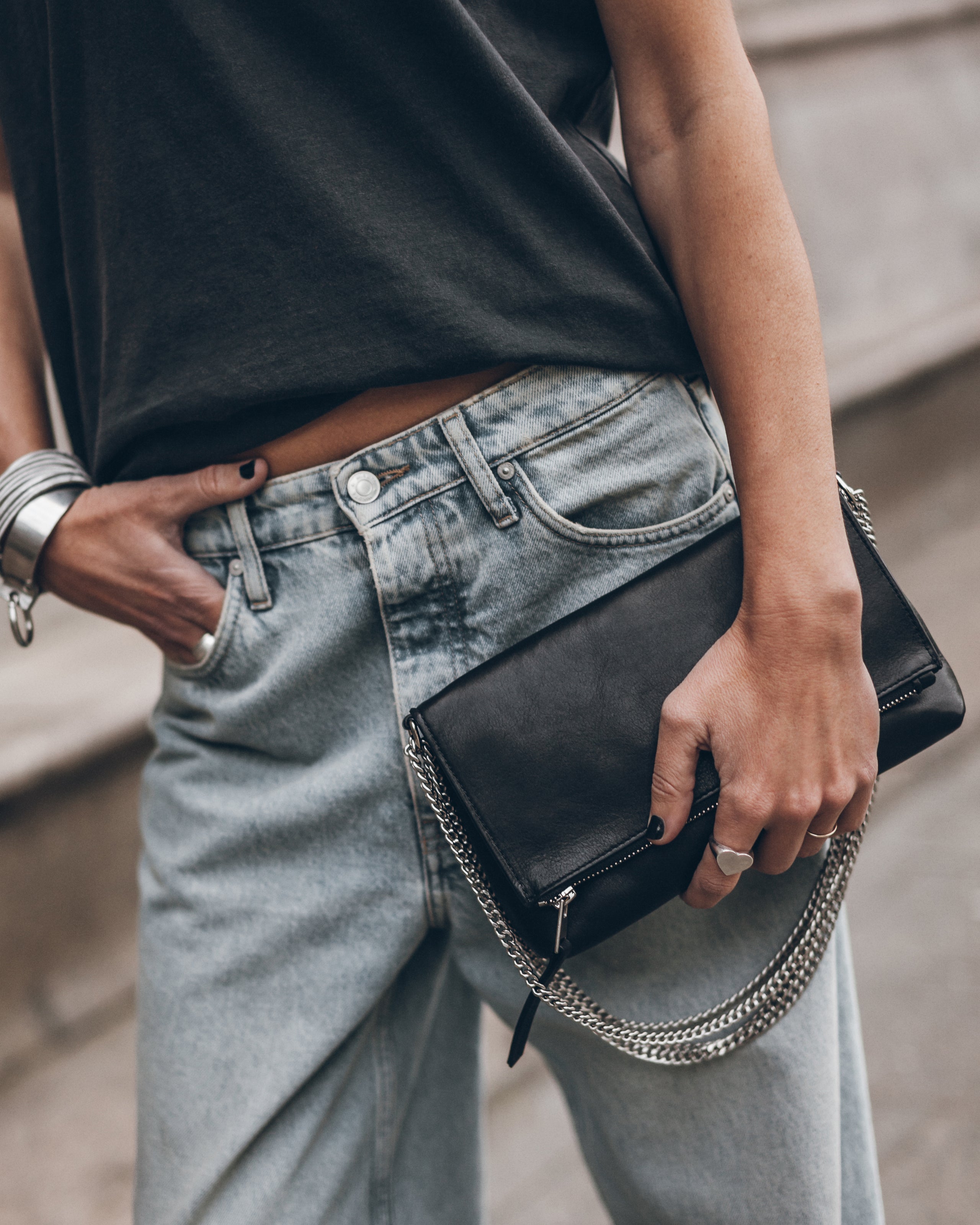 Person wearing a black t-shirt and light blue jeans, holding a black clutch with a chain strap.