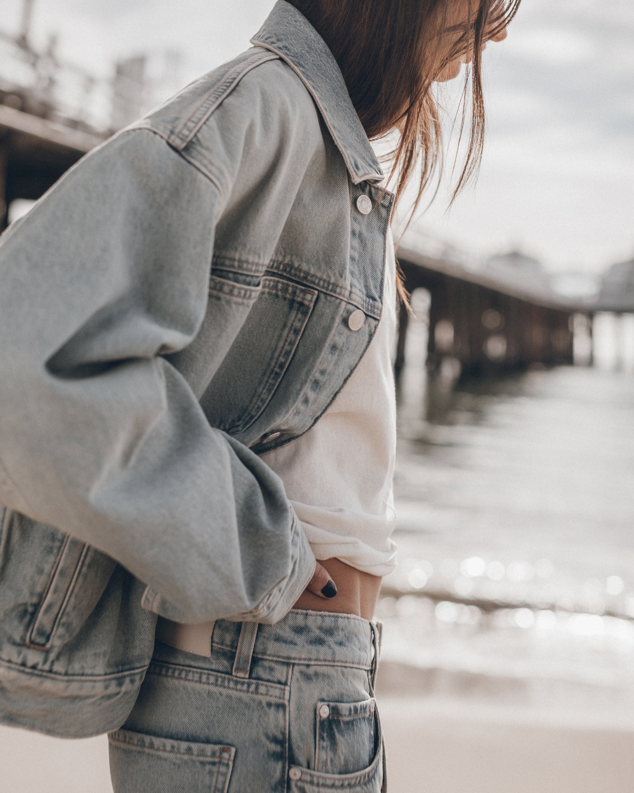 Person wearing a denim jacket and overalls standing outdoors