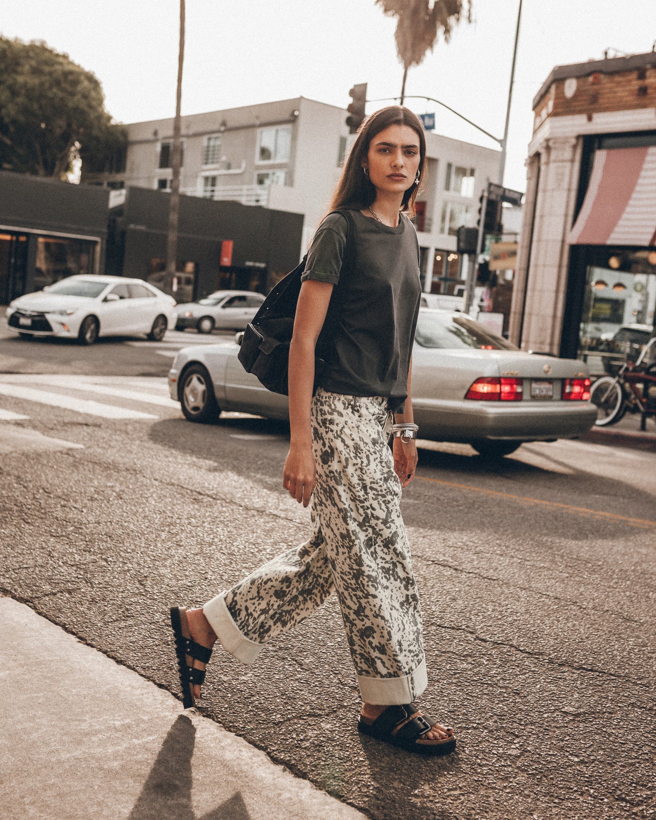 Person walking on a city street wearing a green shirt and patterned pants.