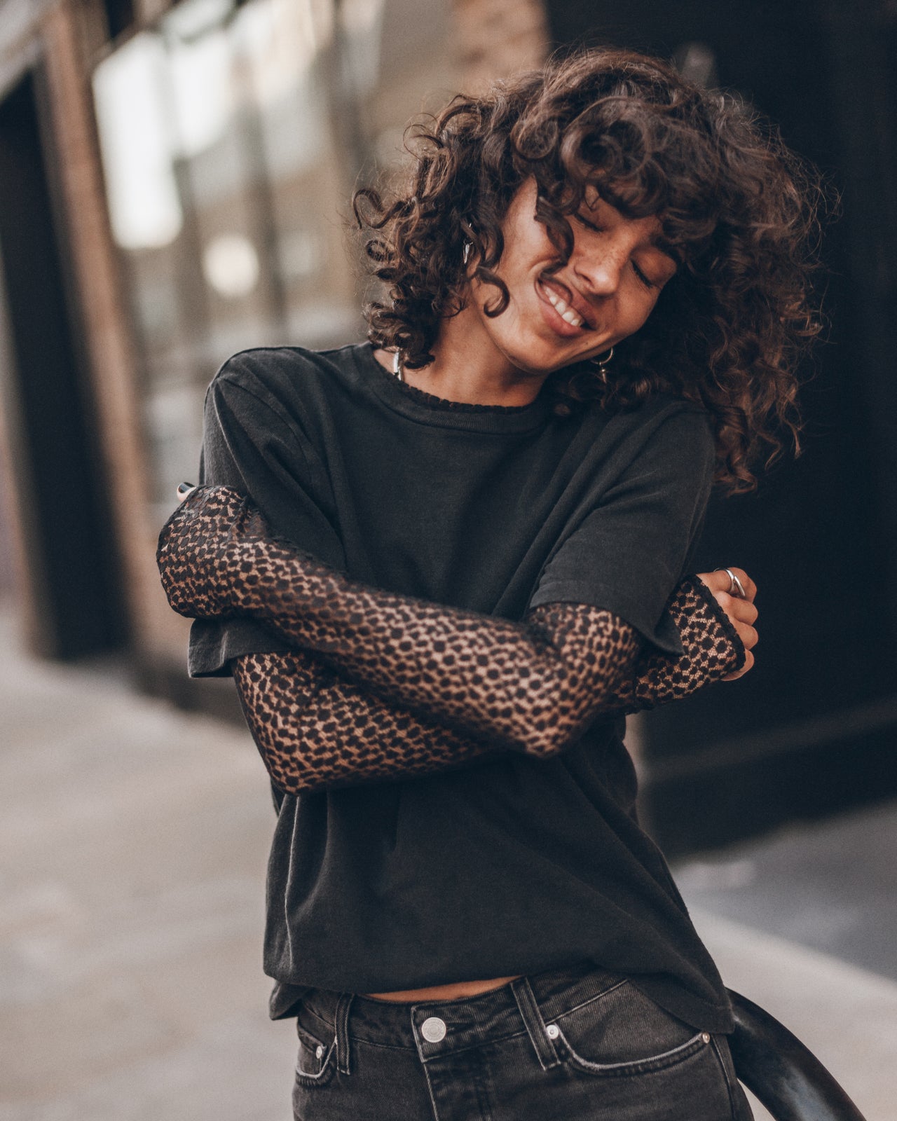 A woman wearing a black crewneck t-shirt, a black lace long-sleeve and black denim jeans.
