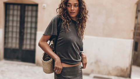 Woman in a gray outfit standing on a stone pavement with a building in the background