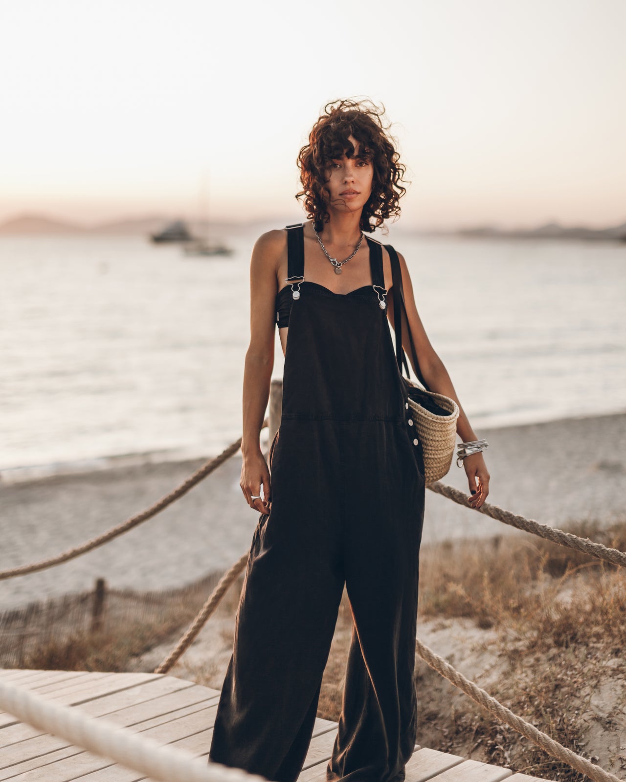 Woman in a black jumpsuit standing on a wooden platform by the water.