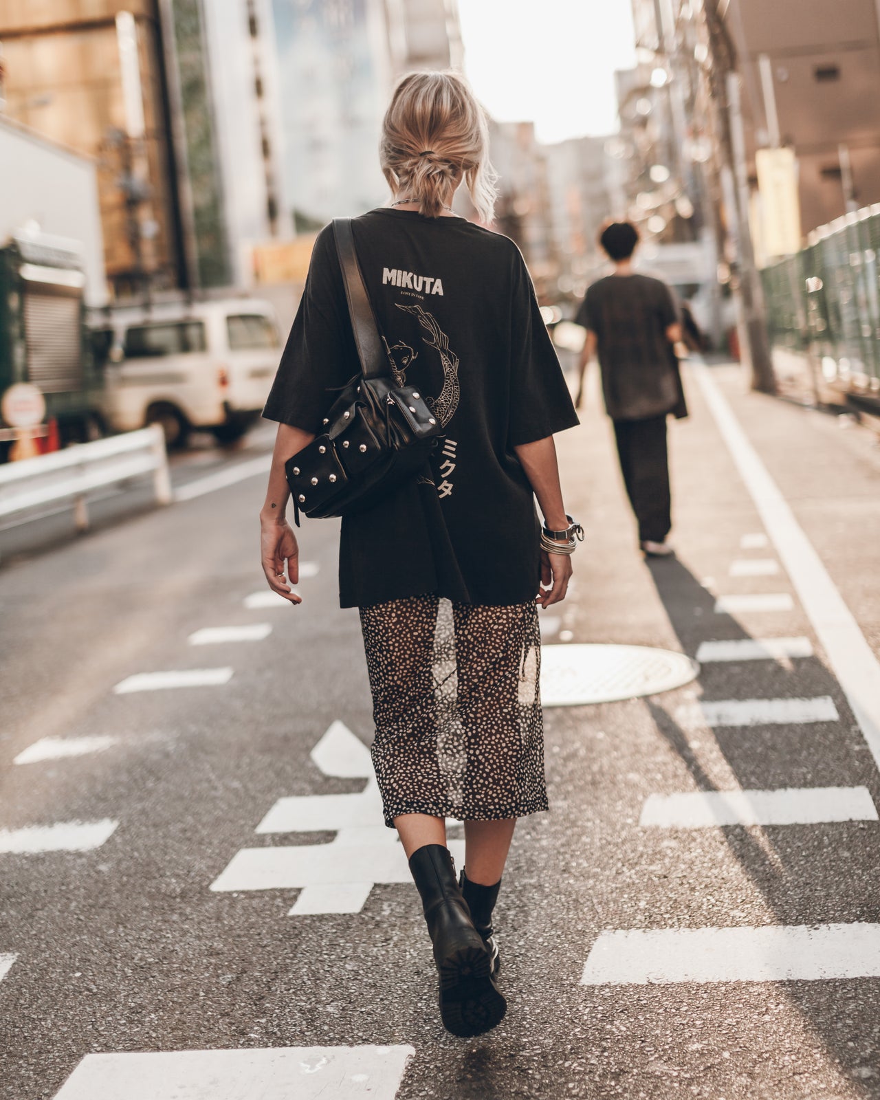 Person walking on a city street wearing a black oversized t-shirt and patterned skirt.