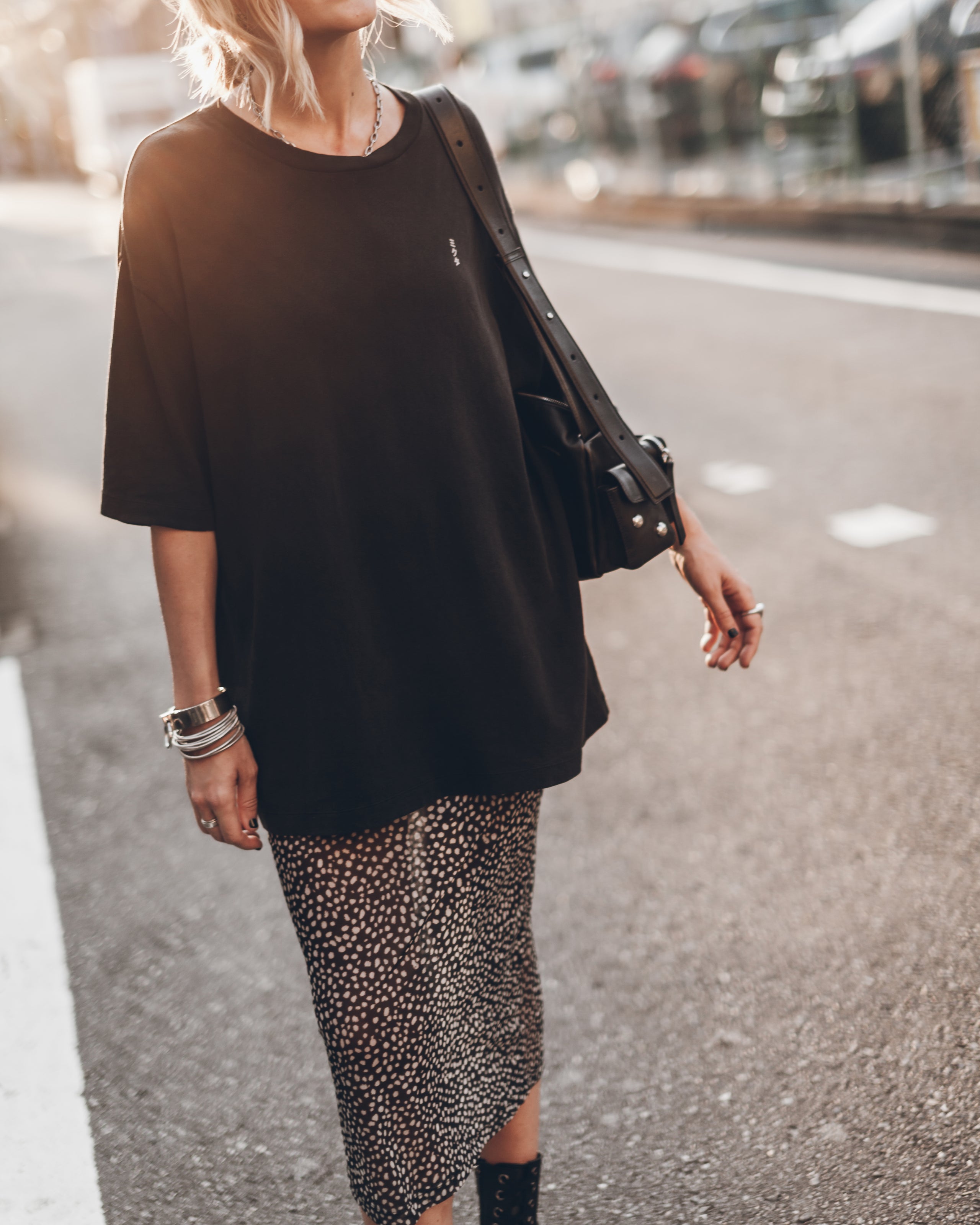 Person wearing a black oversized top and leopard print skirt on a street.