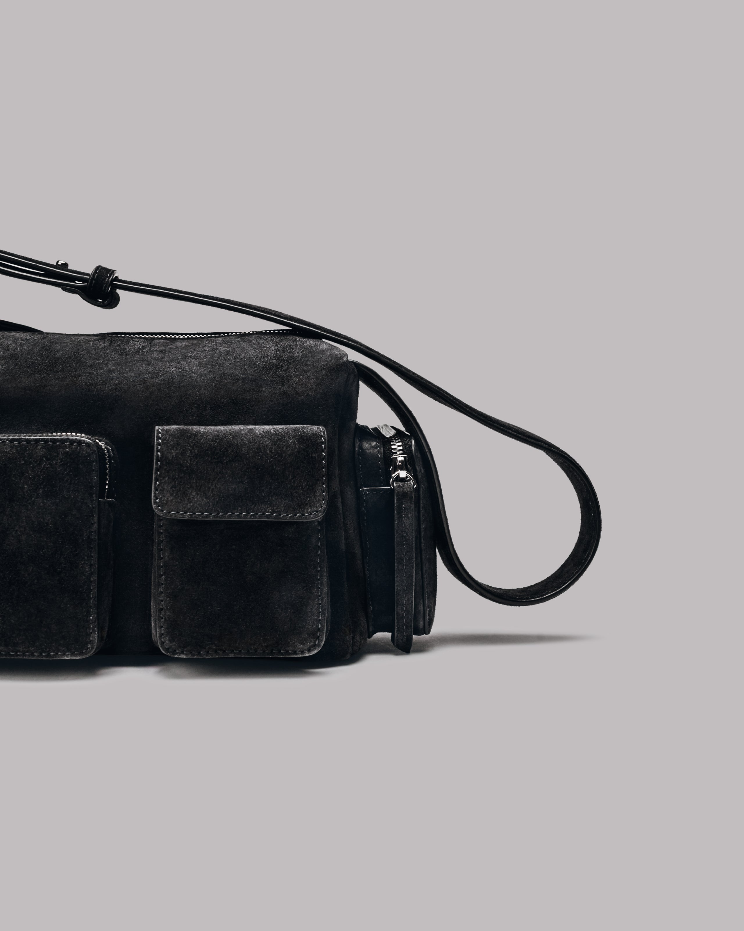Dark suede handbag with a strap on a gray background