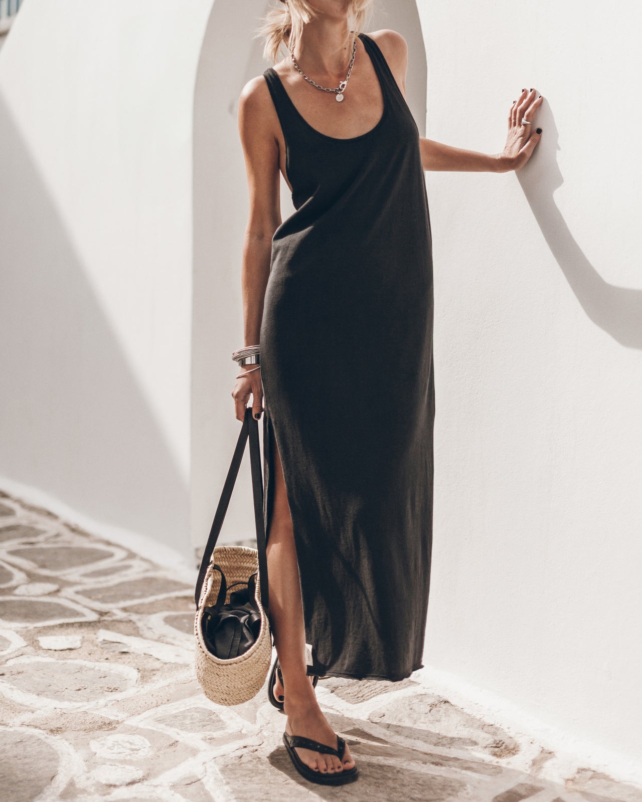 Woman in a black dress holding a straw bag on a stone floor.