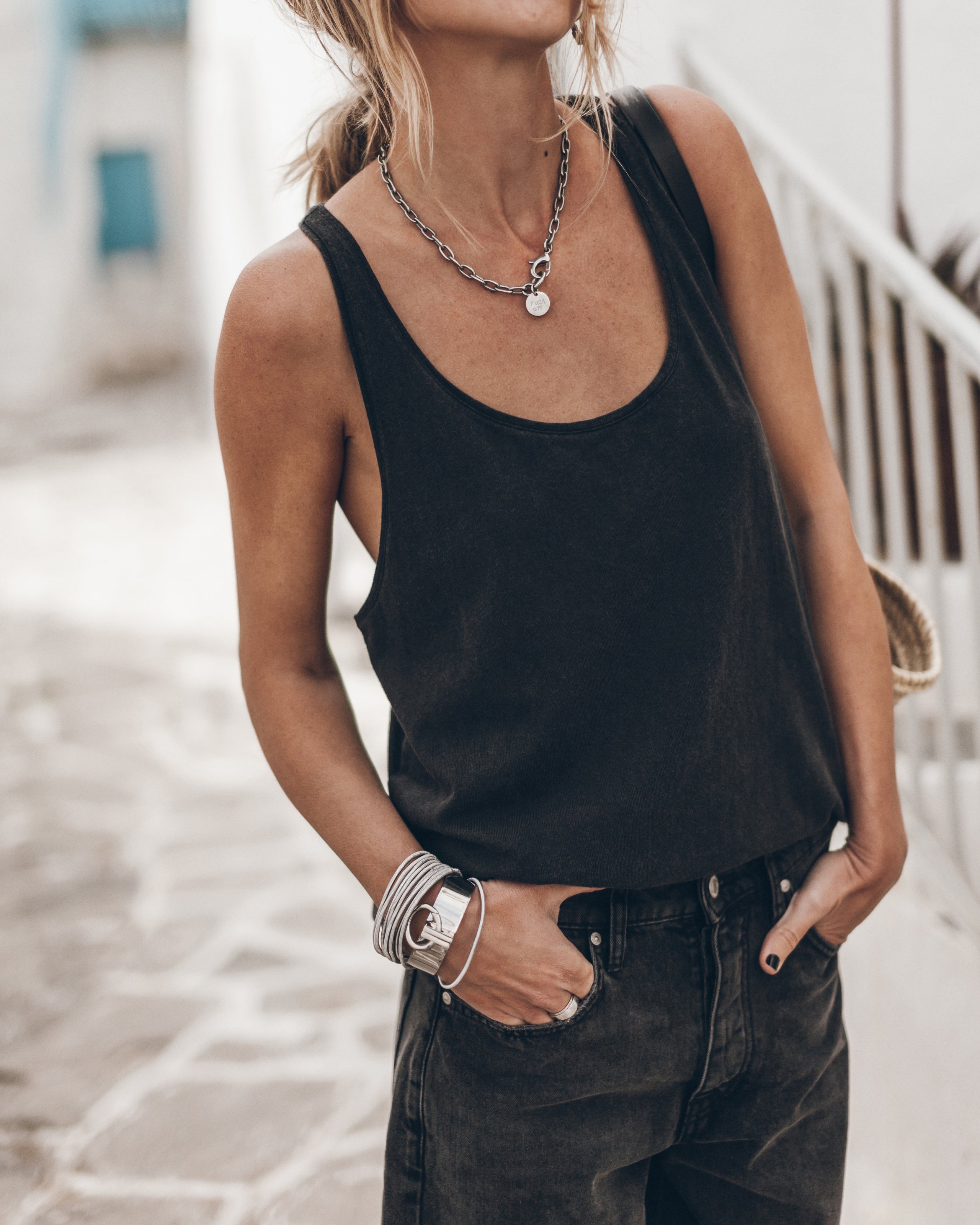 Woman wearing a black tank top and dark jeans, with a necklace and bracelets.