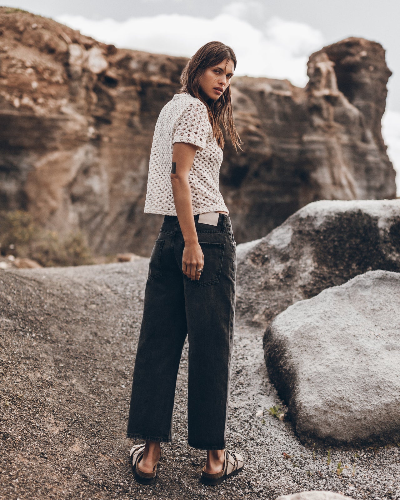 Woman standing on a rocky landscape with large rocks and a cloudy sky.