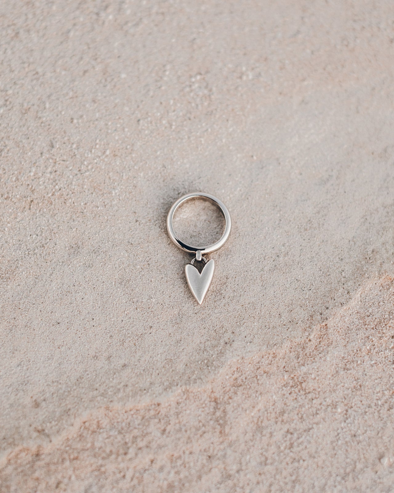 Silver ring with a heart-shaped pendant on a beige surface