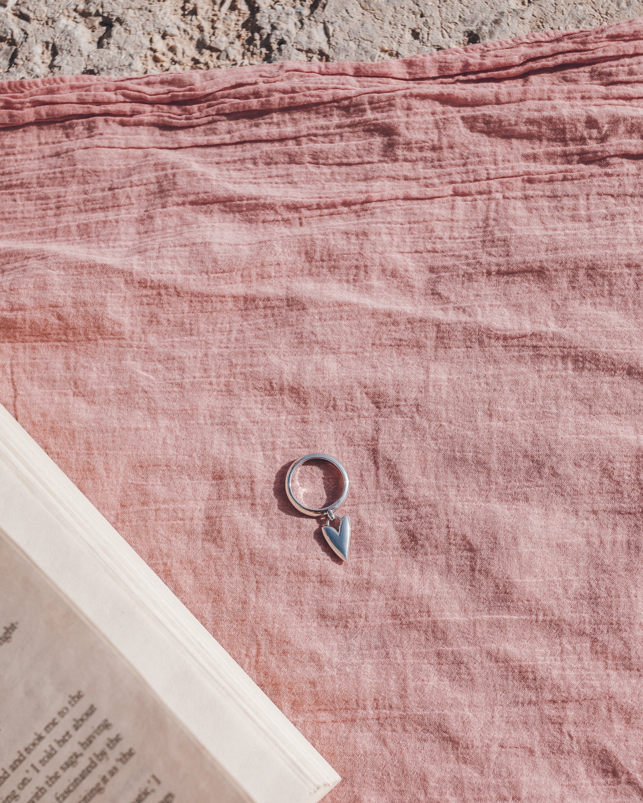 Silver ring with a heart-shaped pendant on a pink pareo